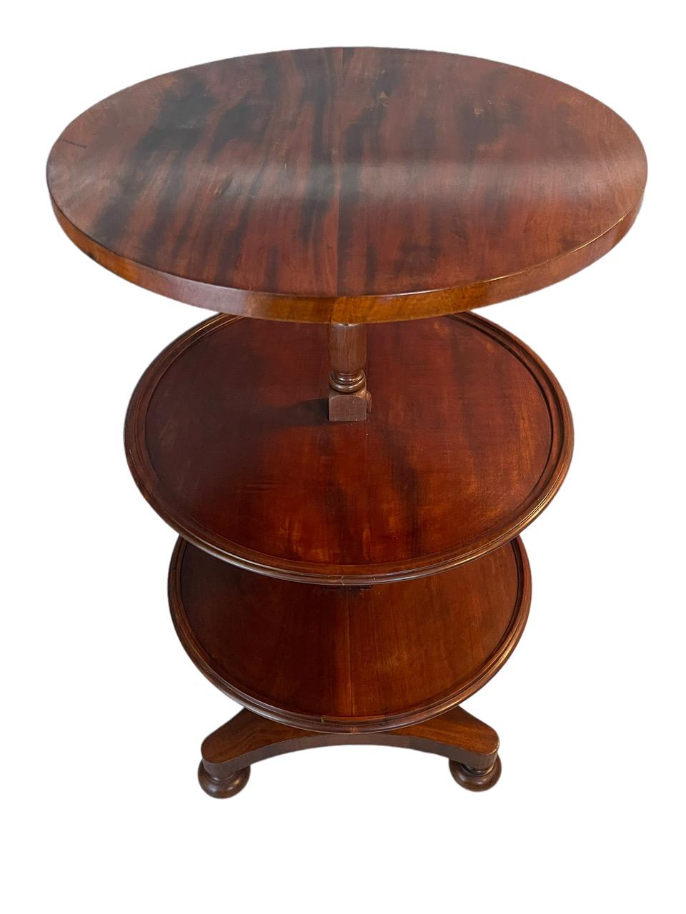 englischer Mahagoni-Tisch aus dem 18. Jahrhundert, erweiterbar, rund, dreistufig, mit Speiseaufzug. Der elegant gedrehte Stiel trägt drei gleich große Schalen. Die Tabelle reduziert und erweitert die Anzahl der Ebenen auf eine oder drei. Er steht