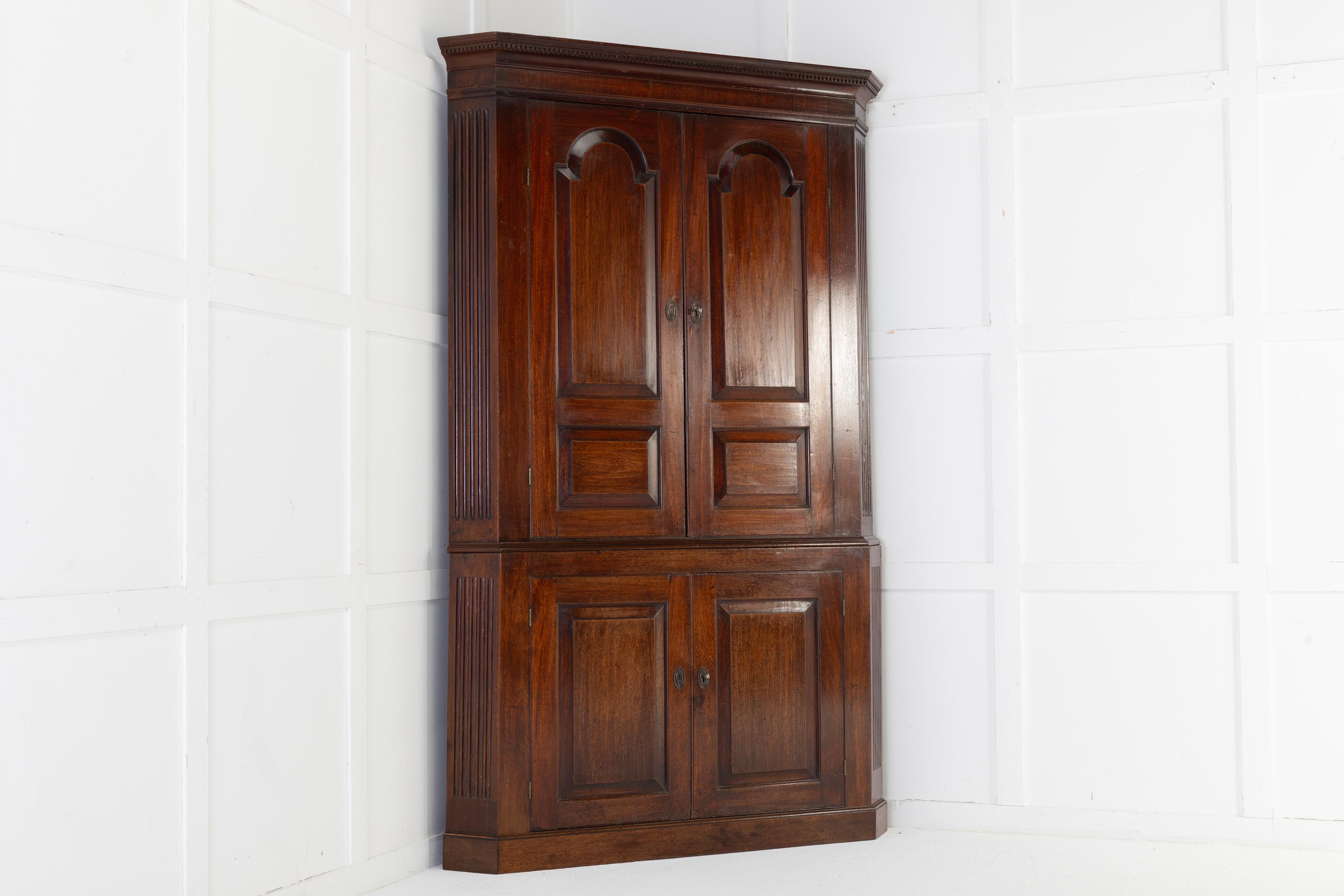 Elegant, English 18th century mahogany, floor standing corner cupboard in two sections. The tall top has a dentil moulded cornice above fielded, arched panelled doors which open to reveal three shaped shelves. The shorter base has two panelled doors