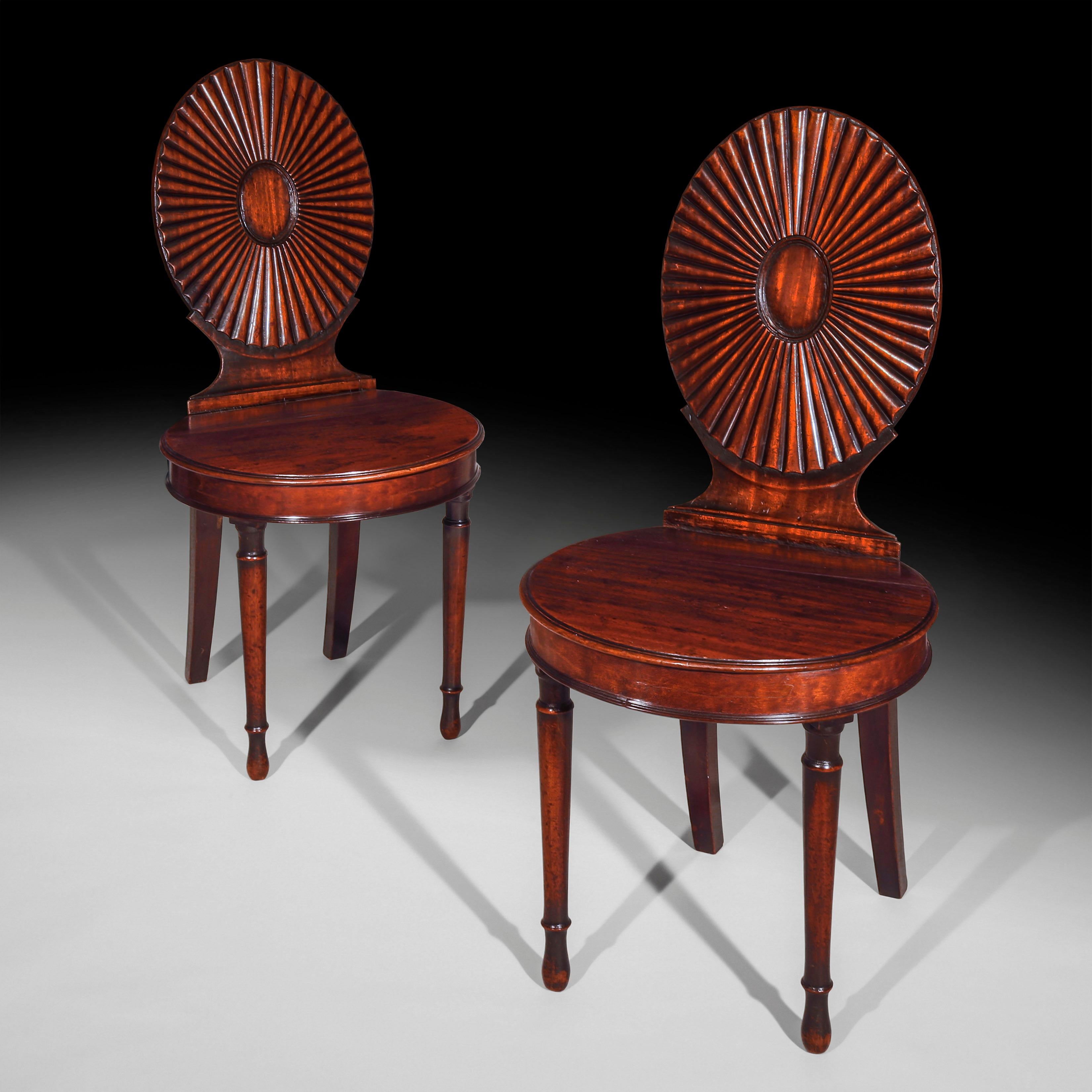 A very fine pair of late 18th century, George III period mahogany hall chairs of the rare neoclassical oval fan-back design, emblematic of the work of the London firm of William Ince and John Mayhew.

English, circa 1780.

Each having an oval