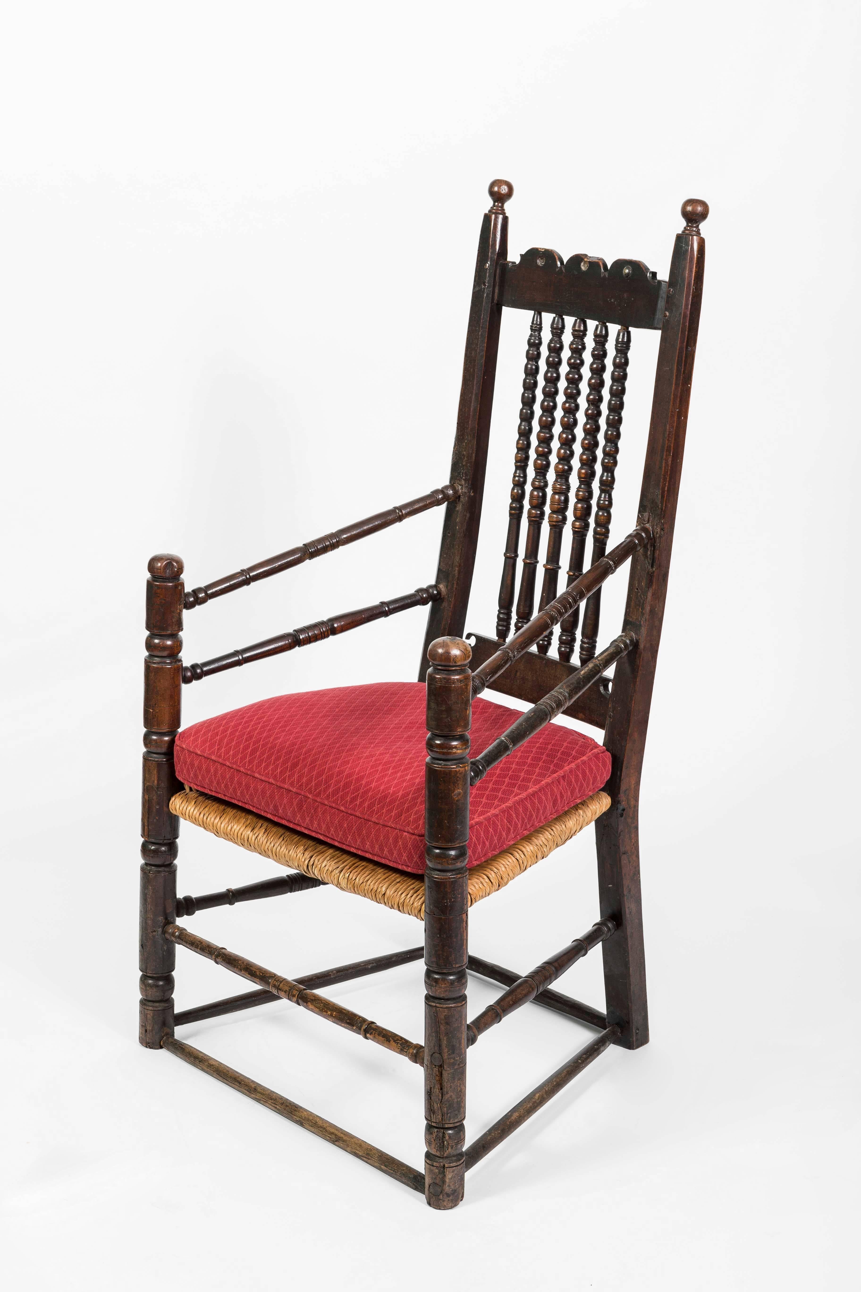 This nice 18th century English oak Bannister armchair has rounded spindles with spools on the back. The base has two sets of stretchers and the arms have two stretches as well. It is fitted with a rush seat.
