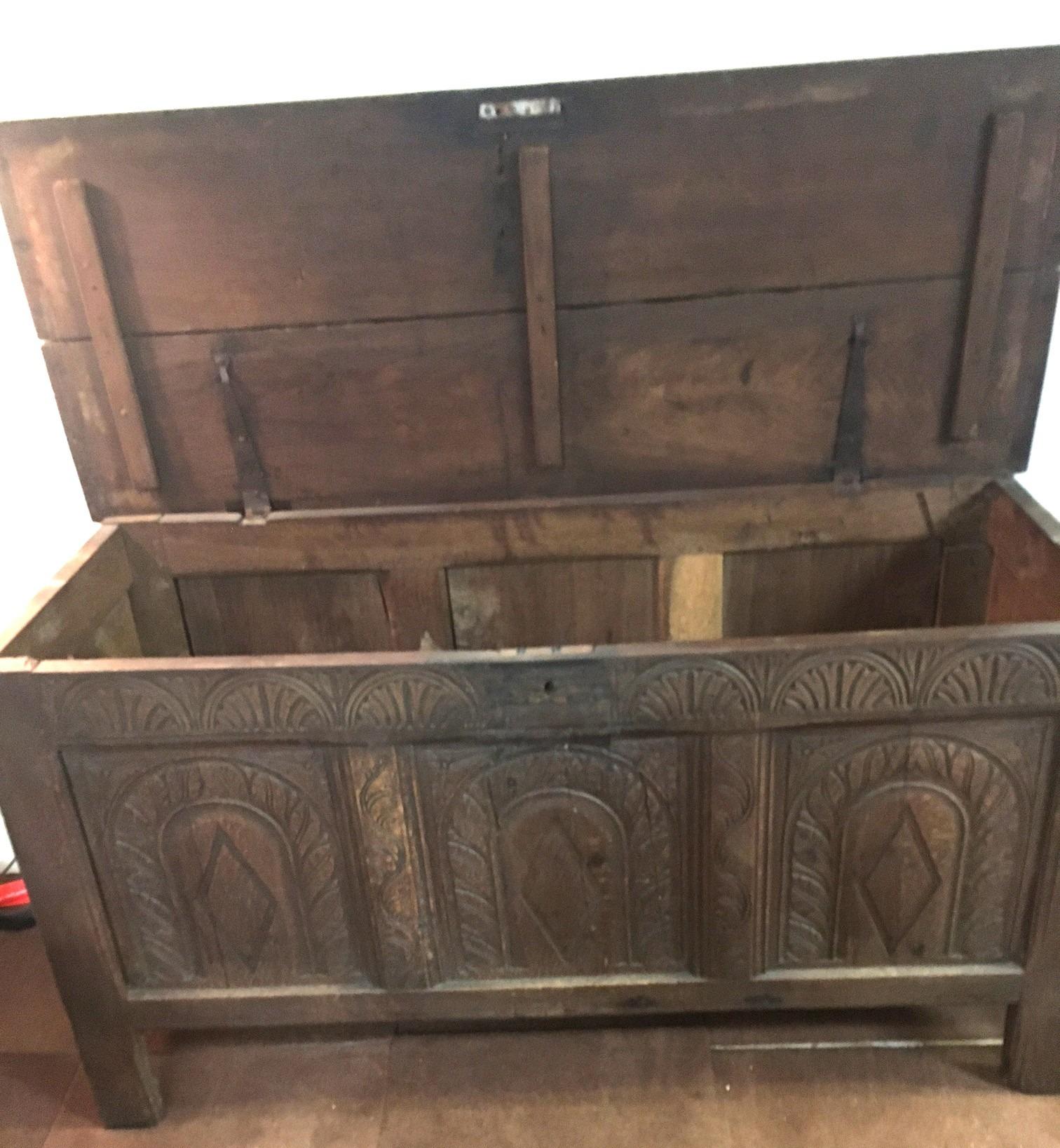 Questo bel forziere in quercia del XVIII secolo con piano incernierato presenta tre pannelli cattedrale intagliati a mano nella parte anteriore e sei intagli demi lune nella parte superiore. Il piano, che poggia su gambe quadrate, è composto da due