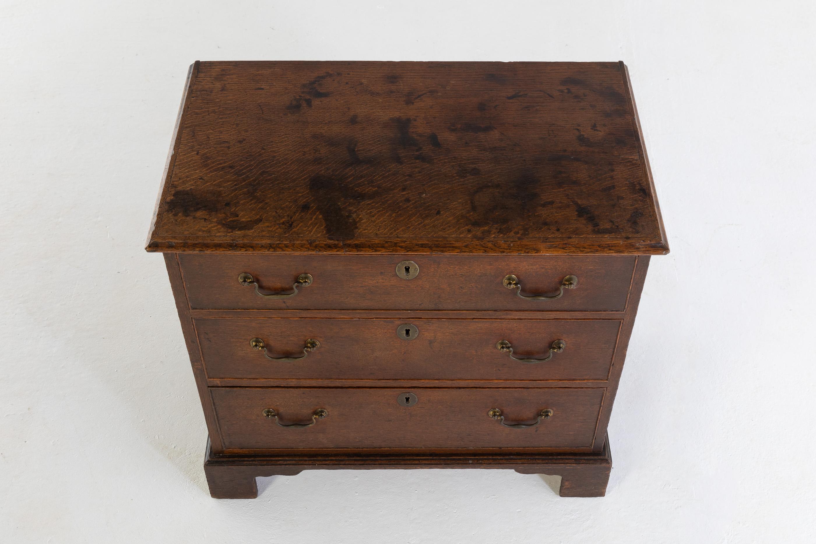 18th century English oak commode. Having moulded top and three graduated drawers with original handles. Standing on carved bracket feet.

Nice small proportion making it an excellent chest for a small room or bedside cabinet.
 