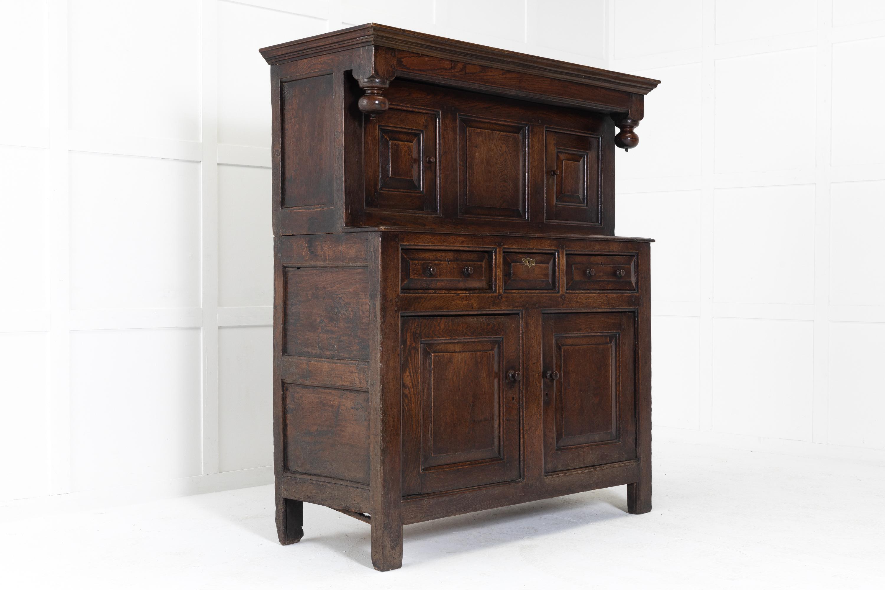 18th English century oak cupboard/dudarn or court cupboard. Having a moulded cornice top above an overhanging frieze. Turned pendant buns with small finials hang at the corners to the upper section, fitted with two panelled cupboard doors. The lower