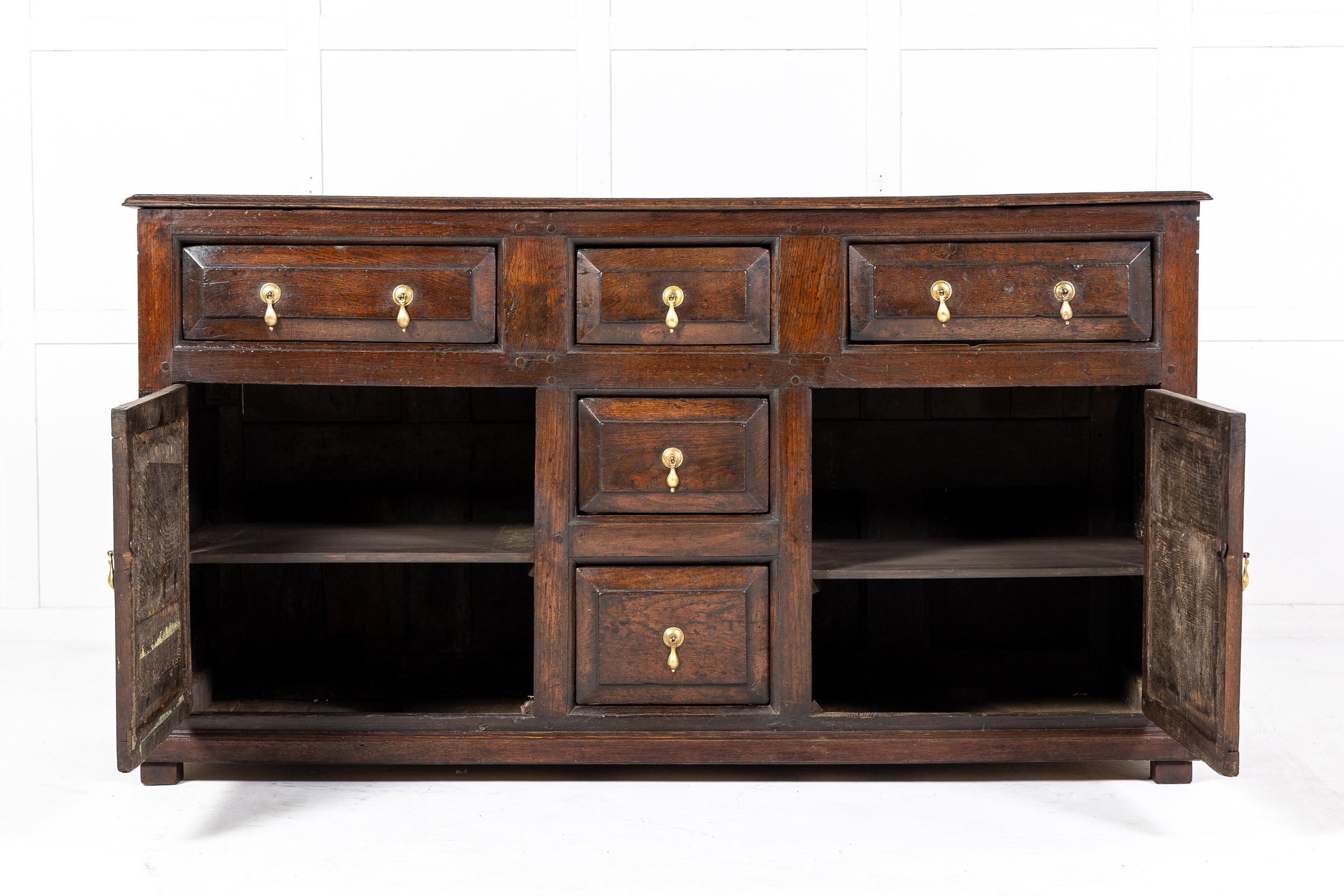 An 18th Century English Oak Dresser Base of Classic Design and Excellent Colour.

The two planked top above an arrangement of panelled cupboard door and drawer fronts, all with brass drop handles. The sides are also finely panelled and the piece