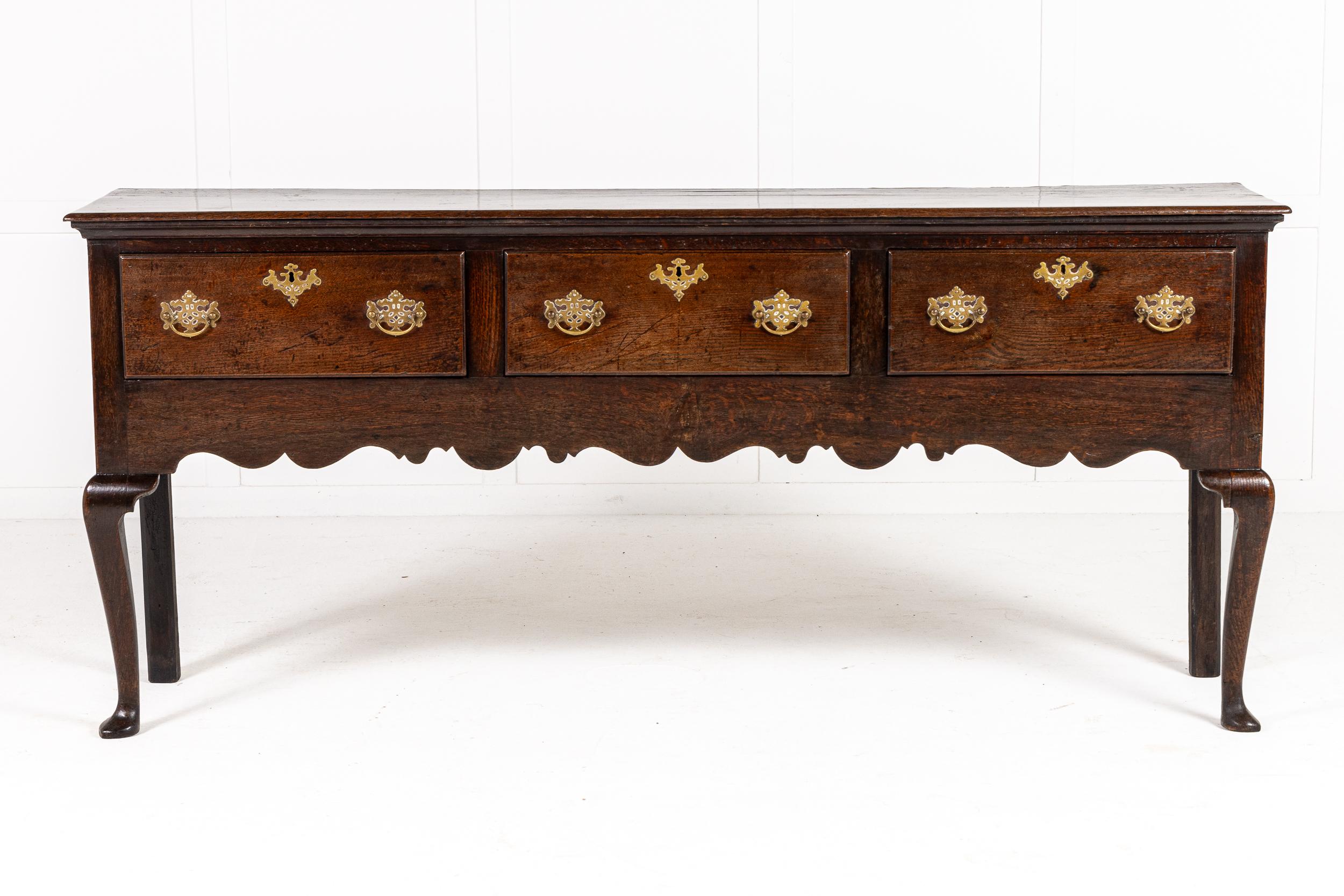 A Good English 18th Century Oak Dresser Base with Shaped Apron.

This three drawer dresser base is an elegant example. Raised on cabriole front legs, it incorporates three drawers, with their original brass plate handles and shaped escutcheons. The