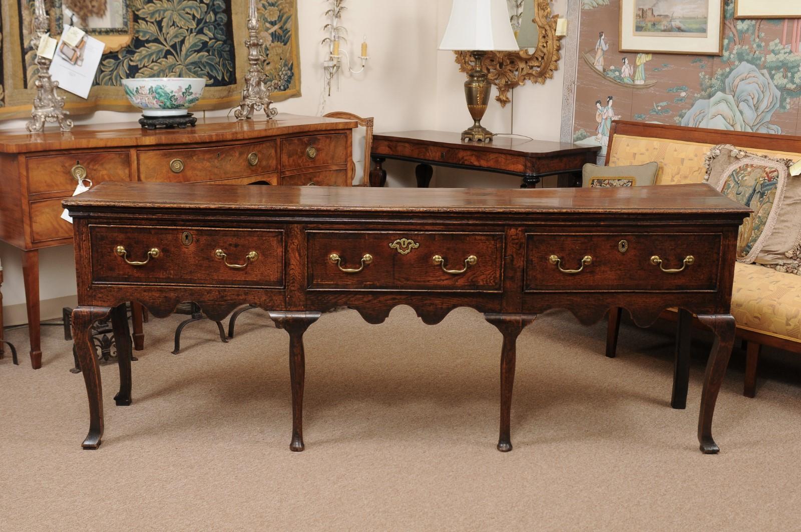 A 18th century English oak dresser base/server featuring 3 drawers, scalloped carved apron, cabriole legs ending in pad feet.