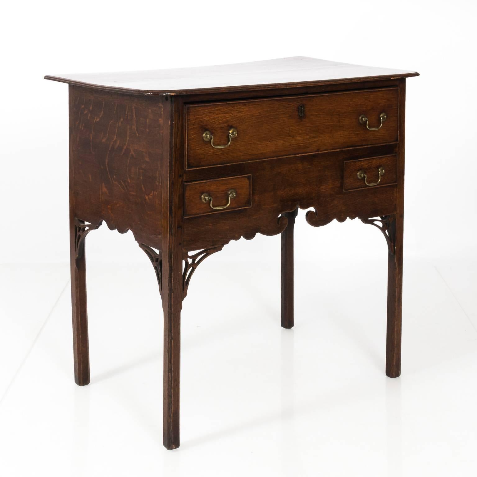 English chinoiserie style oak dresser table with a stylized scrolled skirt, brass handle pulls, and three drawers, circa 18th century. Please note that this piece has minor staining on the table top.
 