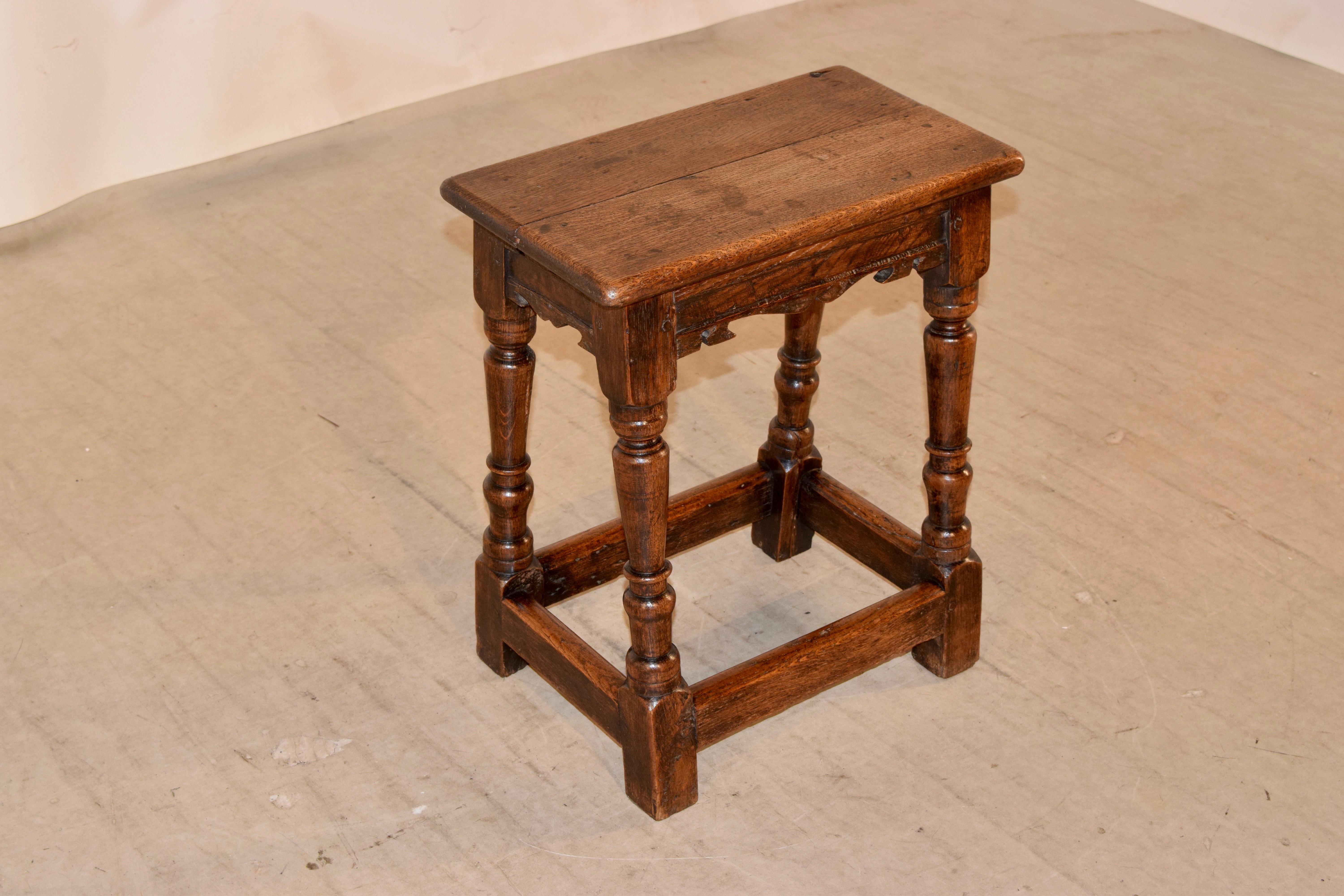 18th century oak joint stool from England with a two board top with rounded edges following down to a lovely hand scalloped apron and supported on splayed and hand turned legs, joined by simple stretchers.