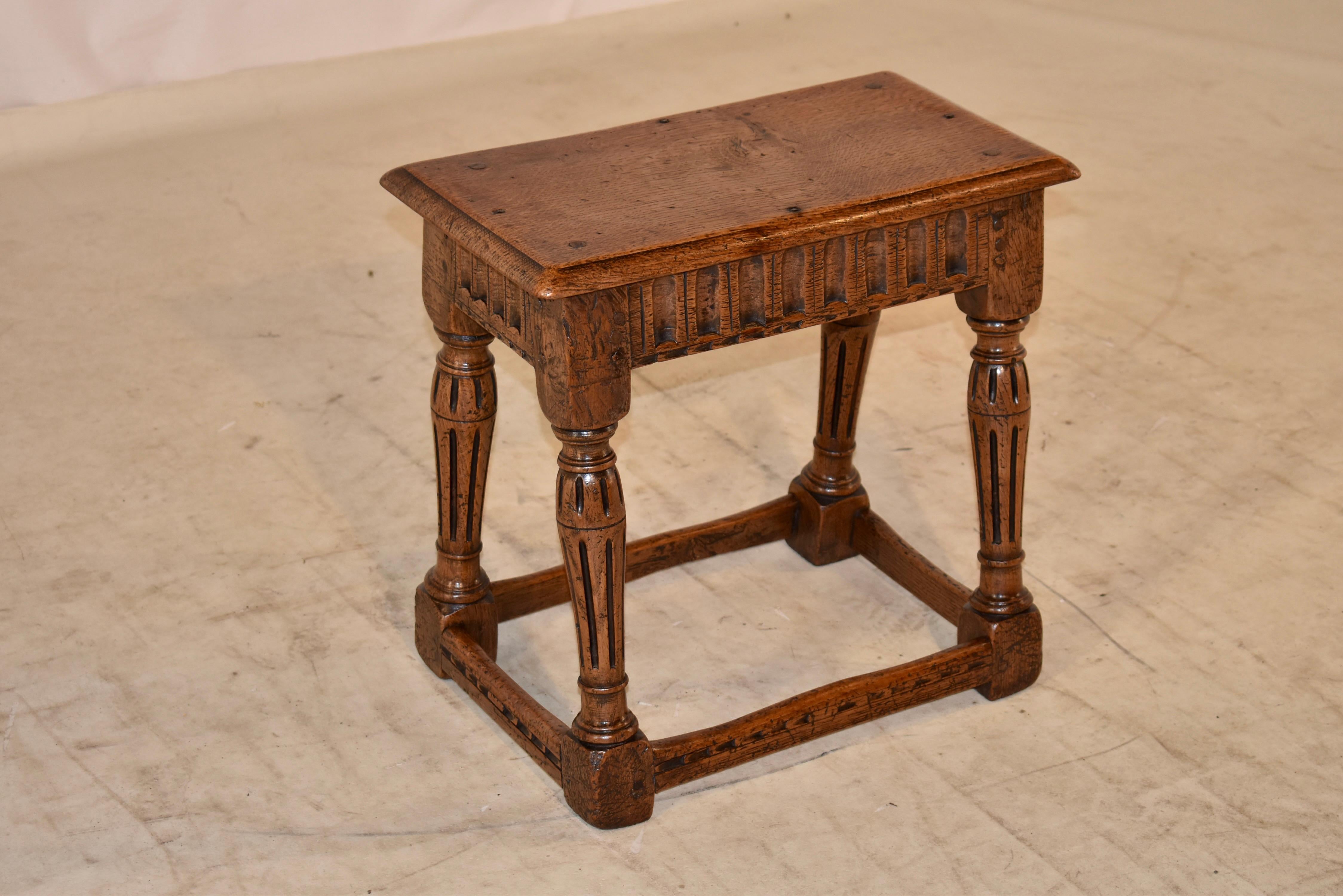 Early 18th century oak joint stool from England with a beveled edge around the top. The top is pegged and secured with hand made rose head nails to the base. The base has a hand carved apron in a nulled pattern, over hand turned and fluted legs,