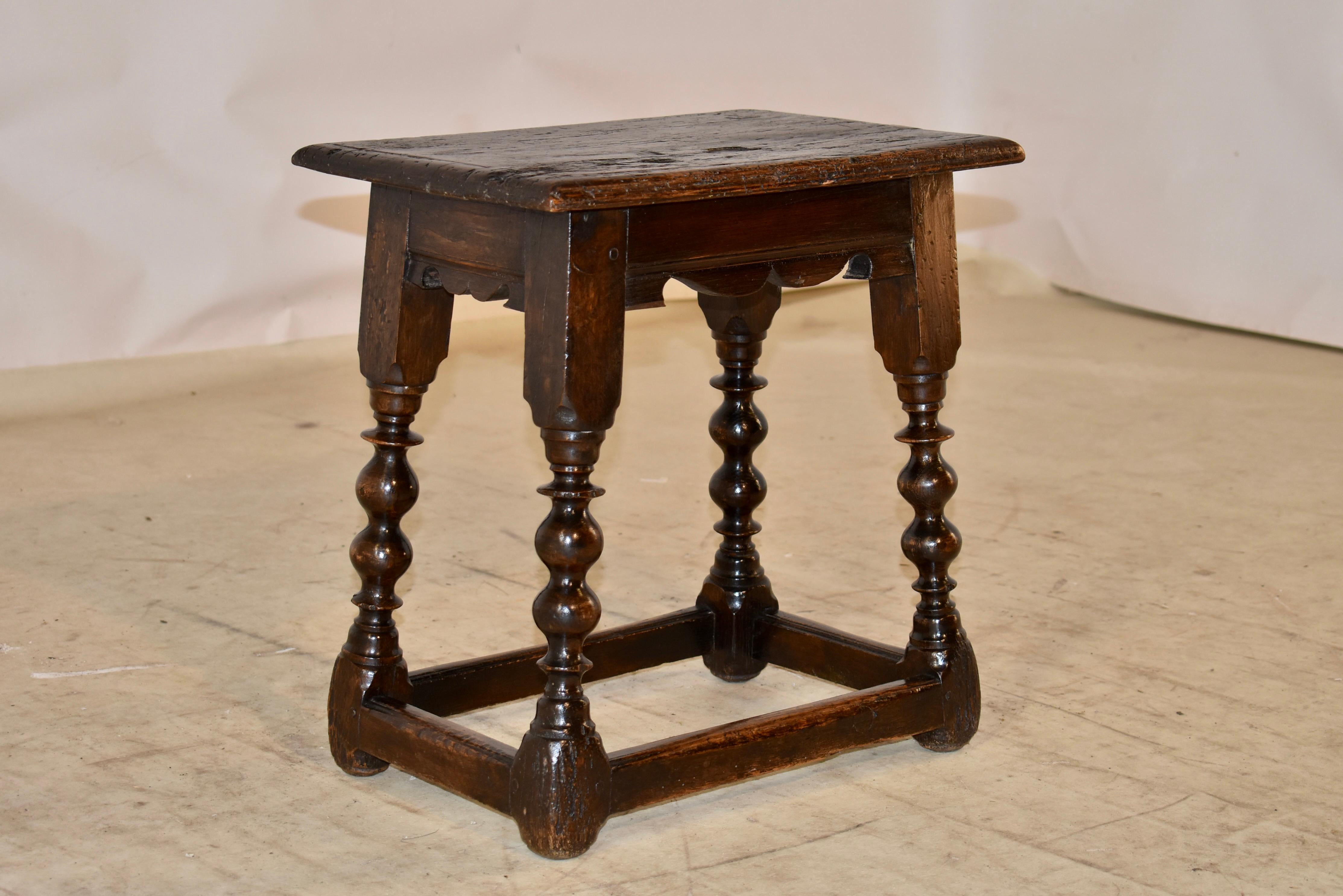 18th century George II period oak joint stool with a well worn top from age and use, which has a beveled edge.  The top is over a scalloped apron.  The stool is supported on hand turned and splayed legs, joined by simple stretchers.  the stool has