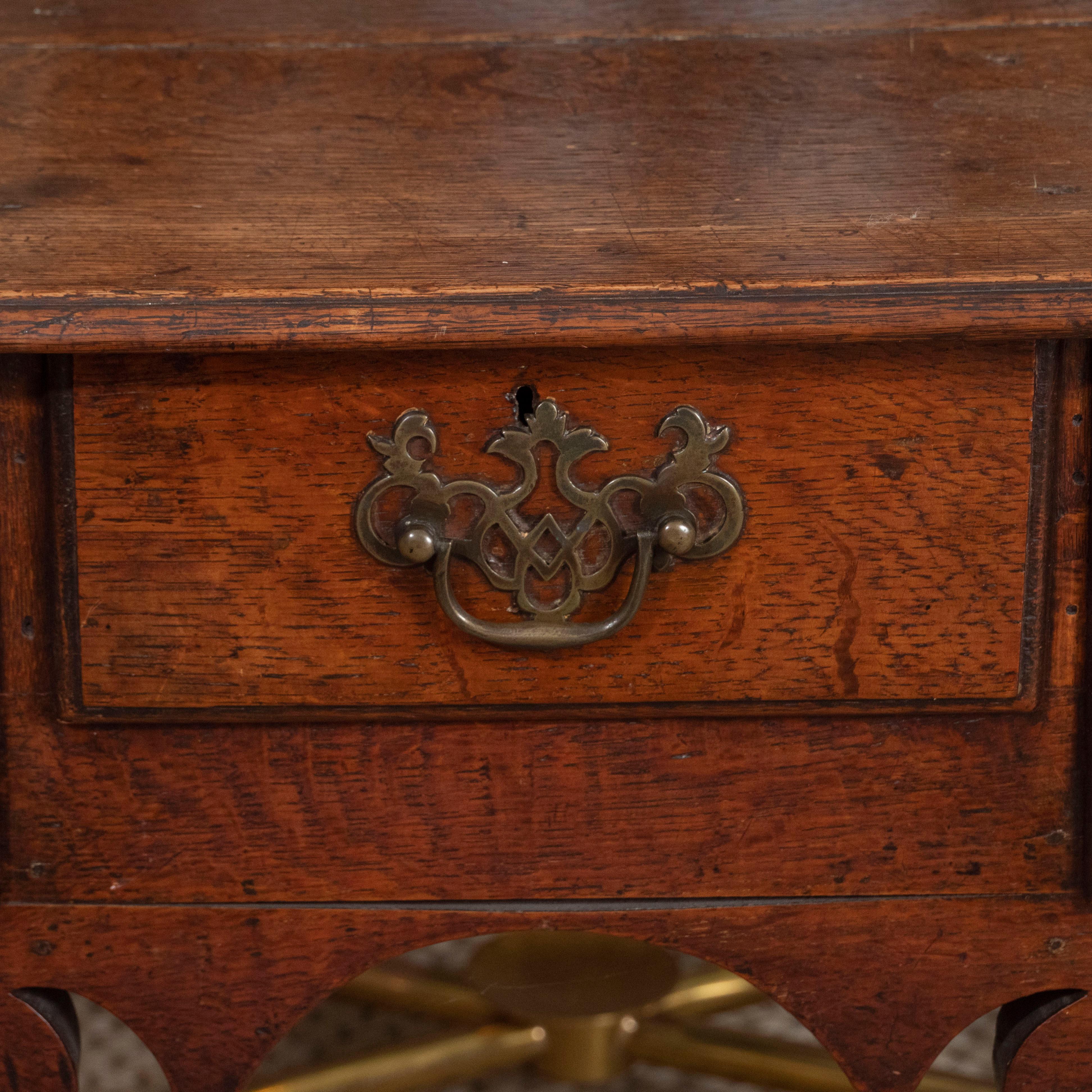 An early 18th century English lowboy dressing table, featuring three short drawers and brass Chippendale-style hardware supported by four legs. The finish has aged to a lovely deep golden brown.