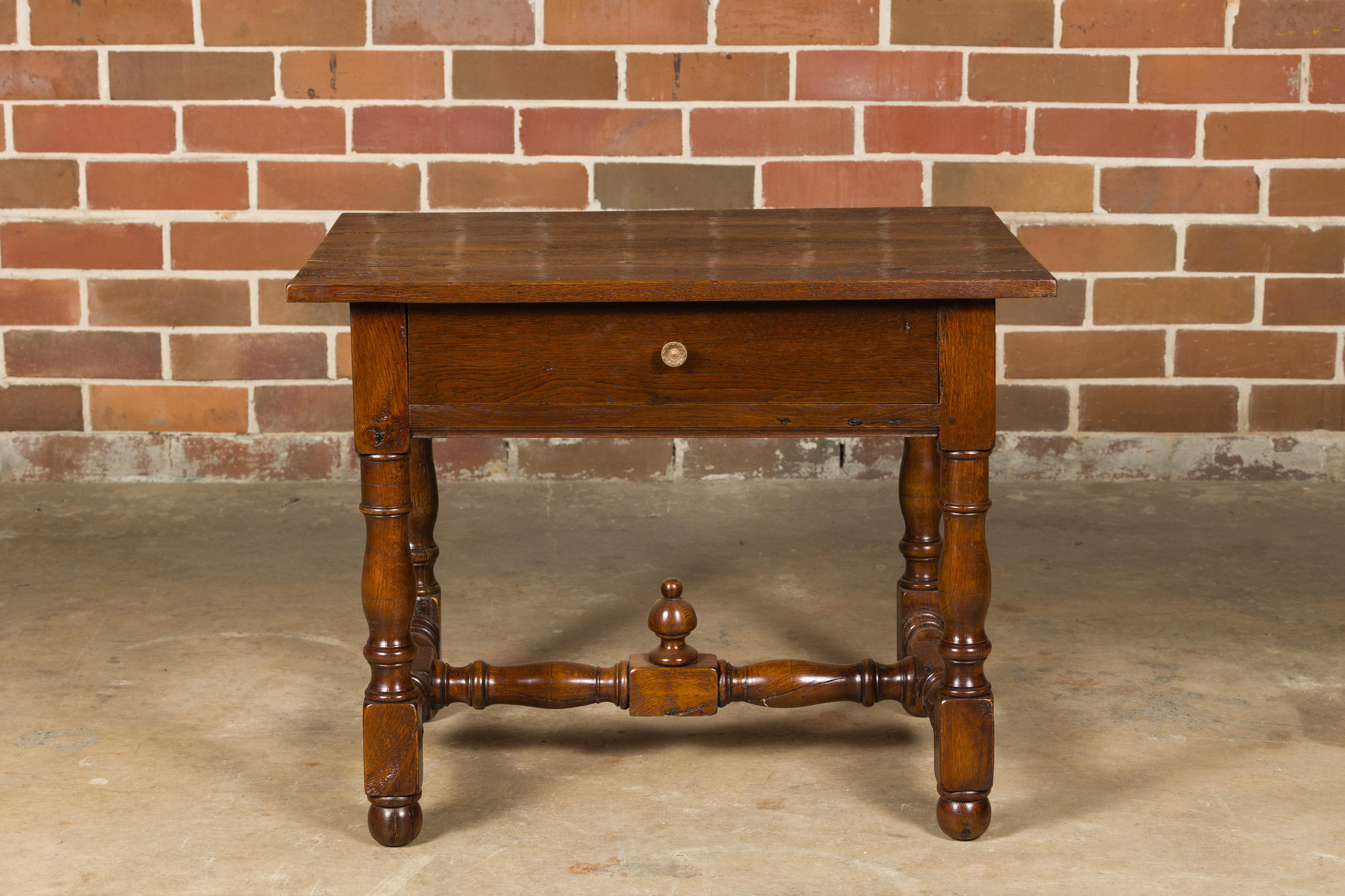 An English oak side table from the 18th century with single drawer, turned base and H-Form cross stretcher with carved finial. This 18th-century English oak side table exudes timeless charm and craftsmanship, making it a delightful addition to any
