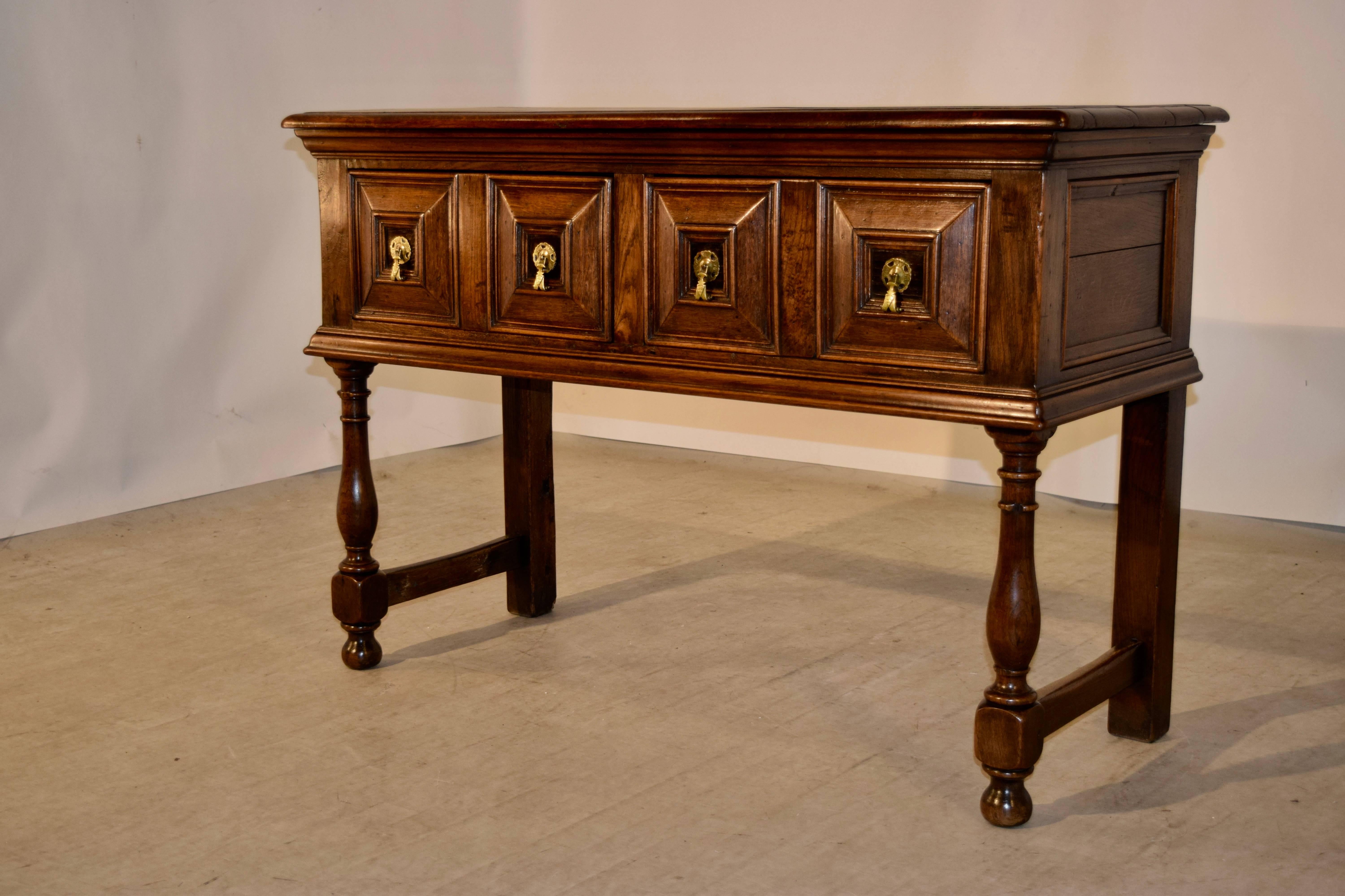 18th century English oak sideboard with a beveled edge around the top, following down to hand paneled sides and two drawers in the front with cushion panels. The piece is raised on hand turned legs in the front and simple legs in the back, joined by