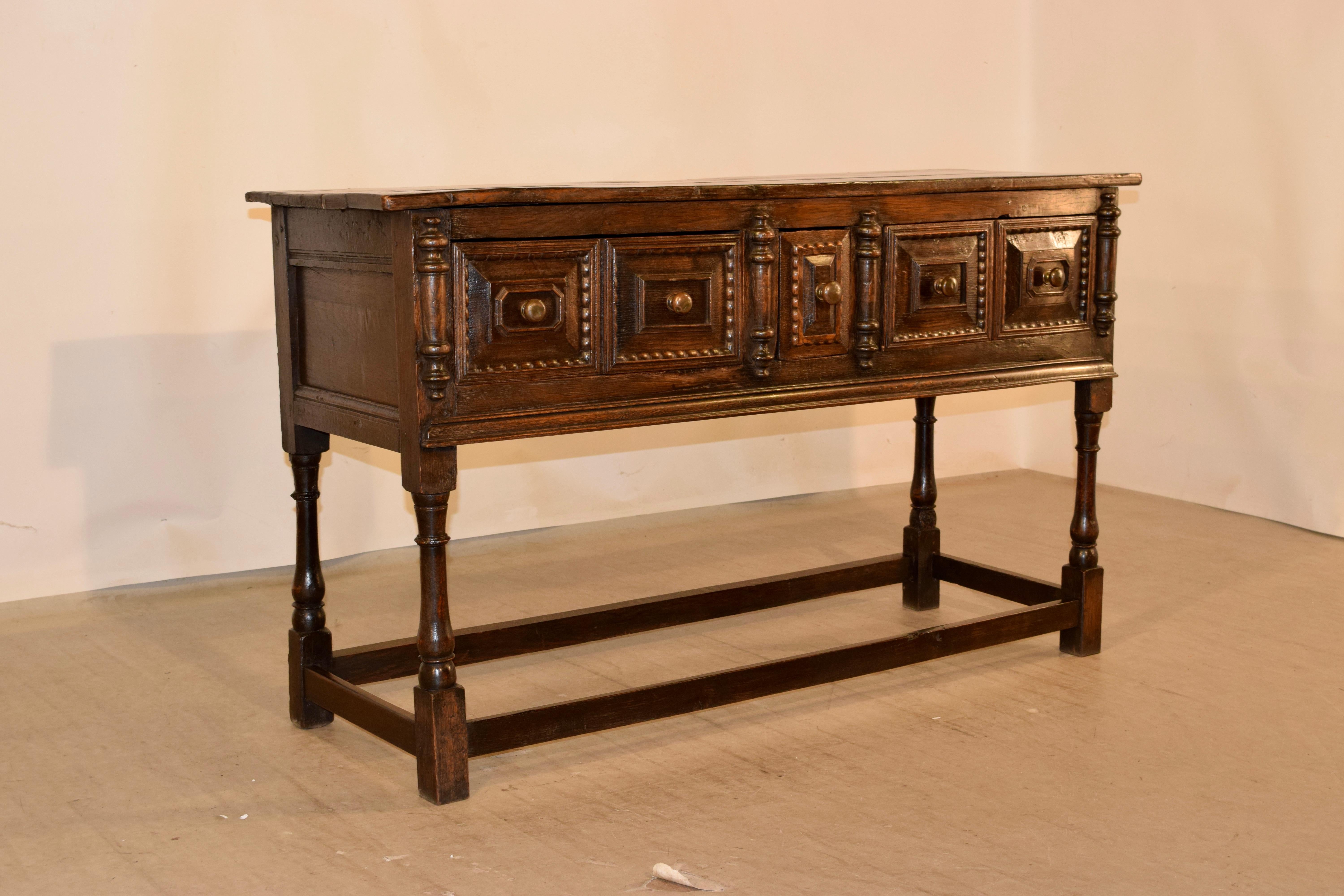 18th century oak sideboard from England with a plank top, following down to hand paneled sides and a single candle drawer in the front, flanked by cushion paneled drawers. There are applied turnings flanking the drawers as well, for added interest.