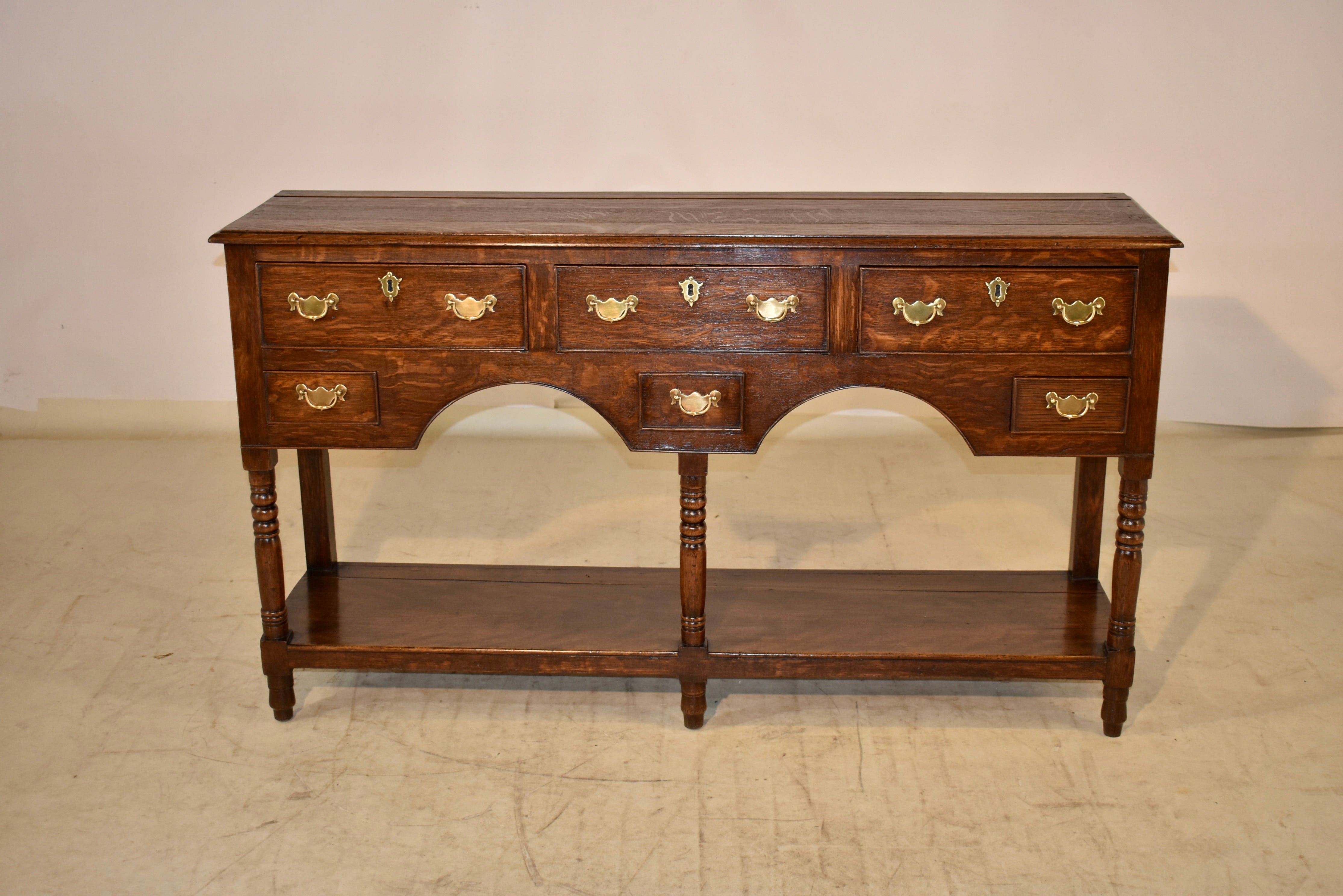 18th century oak sideboard from England with a beveled edge around the top and a plate rail. The top follows down to simple sides and three larger drawers over three smaller drawers in the front of the piece. It is supported on simple legs in the