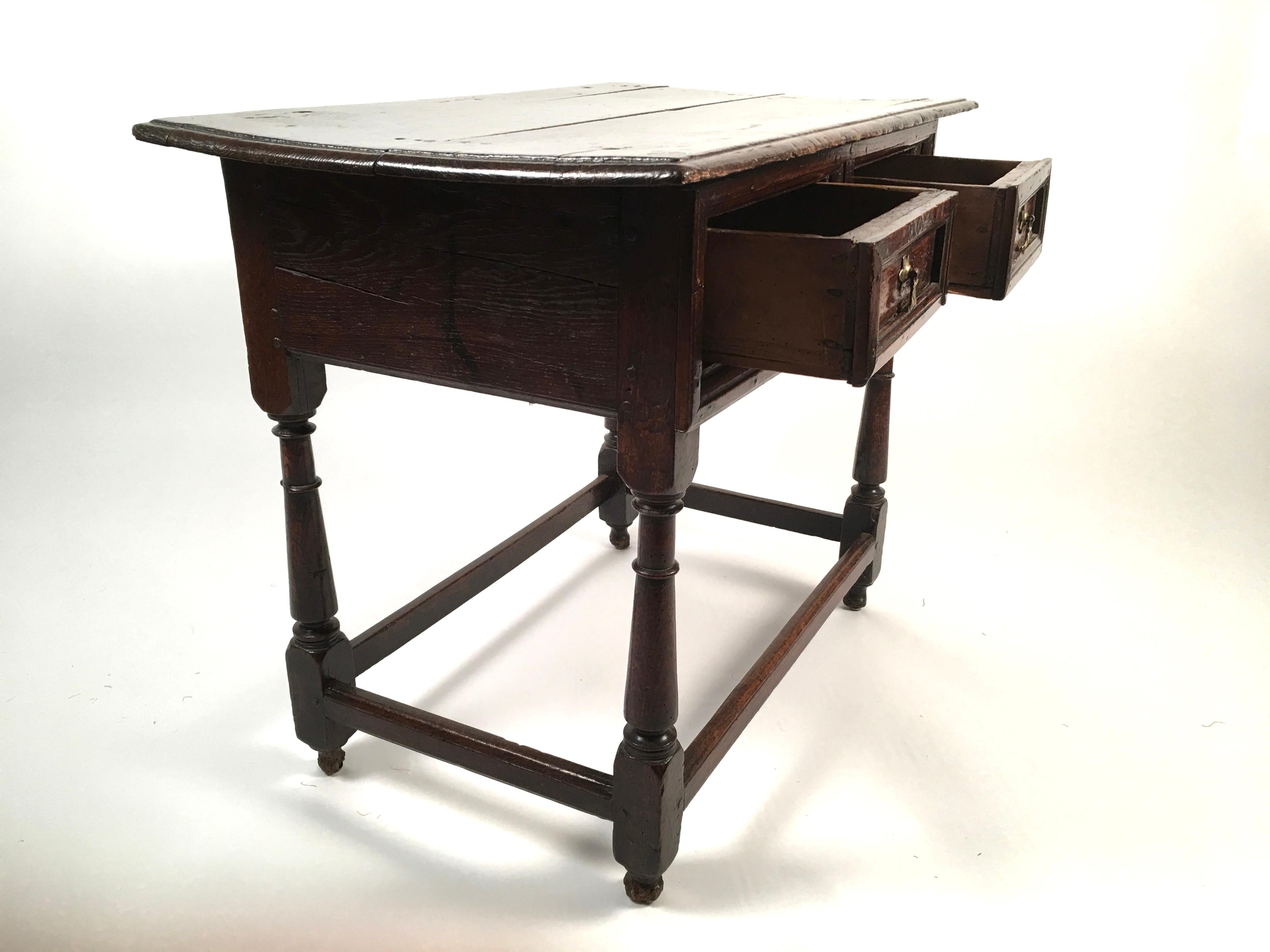 An 18th century English oak tavern table, the rectangular top over two drawers with brass drop handles, raised on four cylindrical, turned legs joined by cross stretchers. Good, rich patina and color.