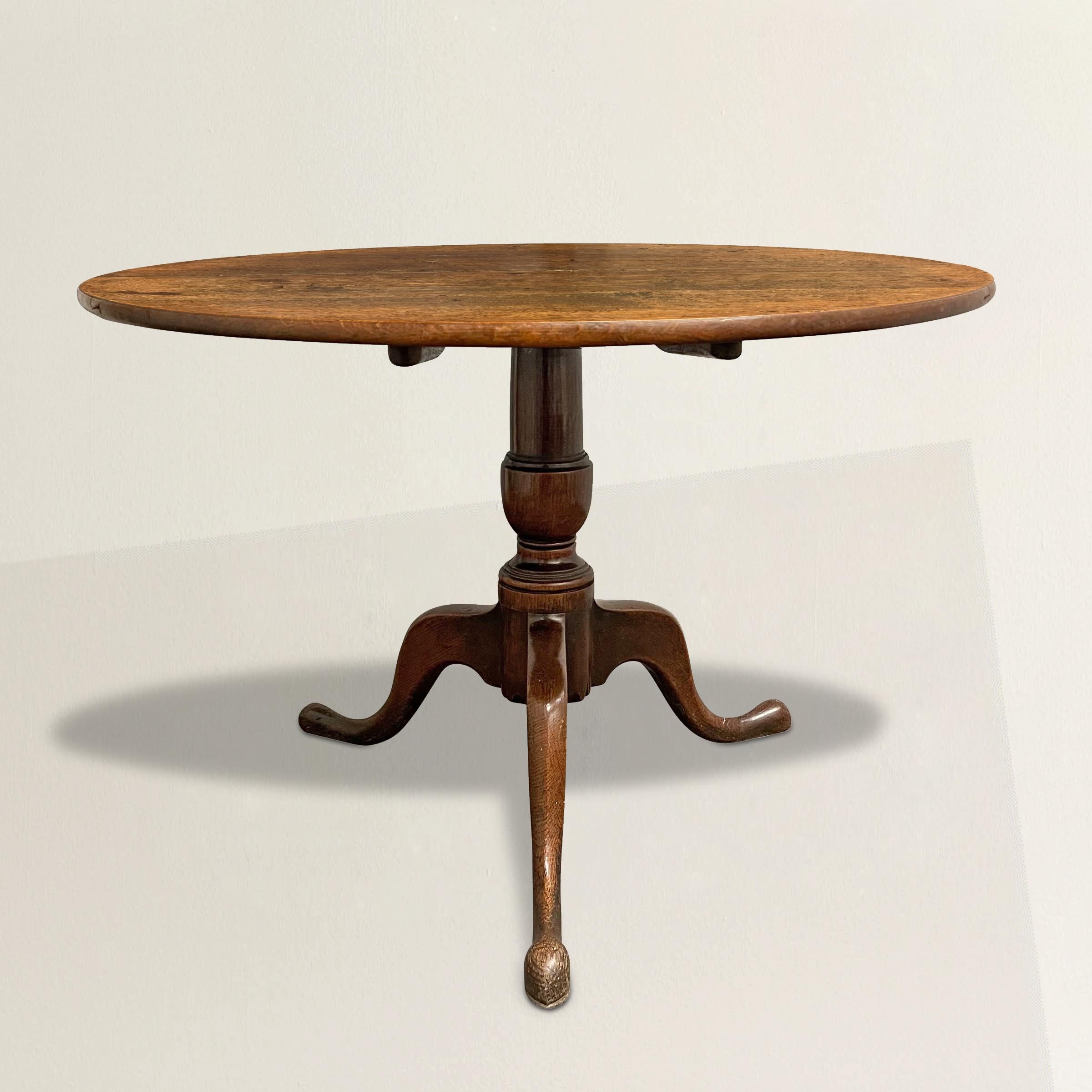 This 18th century English Queen Anne oak tilt-top table is a charming relic from a bygone era, originally designed to serve tea or meals on. Its unique feature lies in the tilting mechanism of the top, which allowed the table to be conveniently