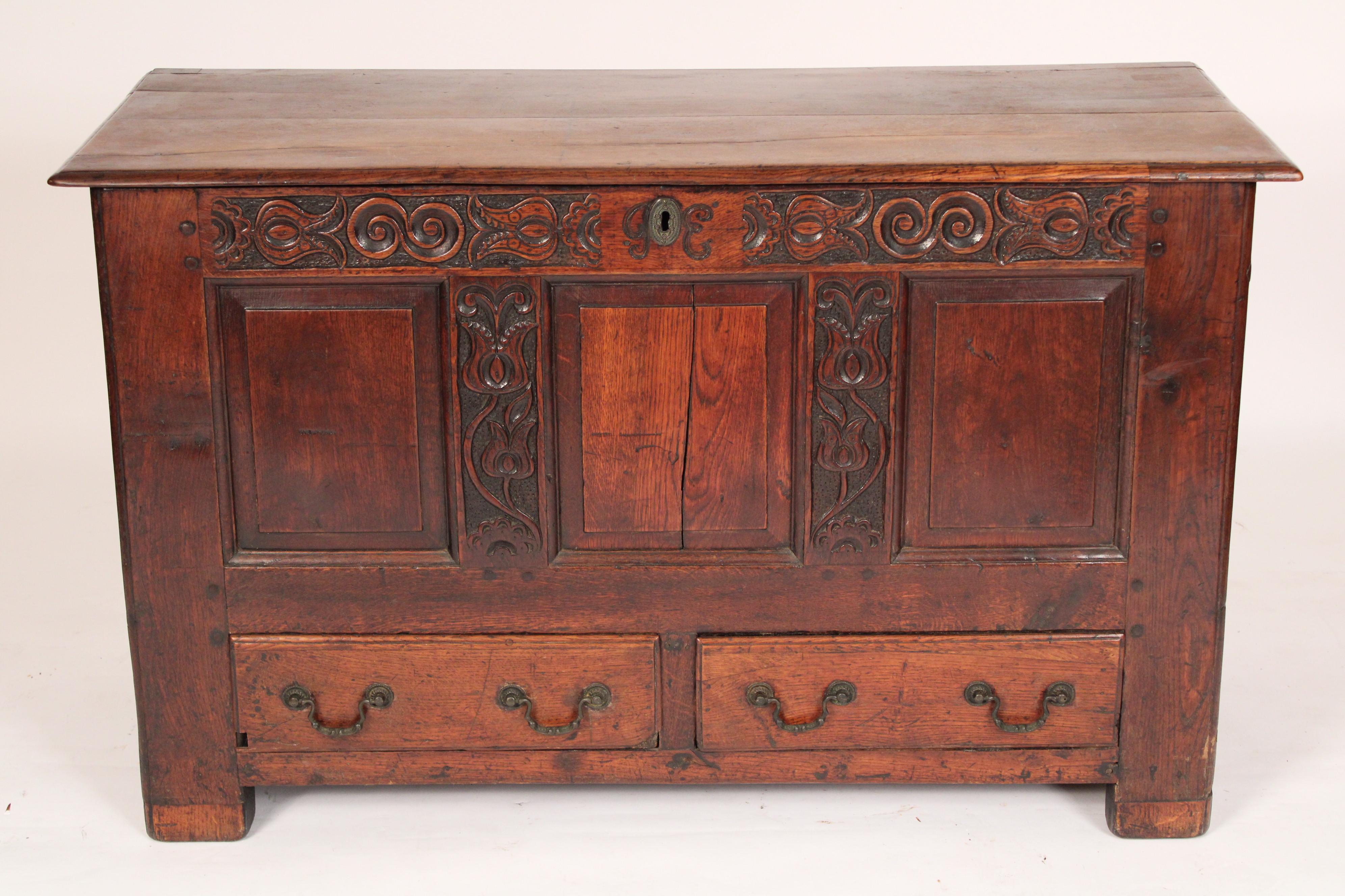 Antique English oak trunk, 18th century. With a rectangular overhanging top, the front with a carved horizontal member with the initials GE over 4 stiles the inner stiles with carvings and two drawers resting on block feet.