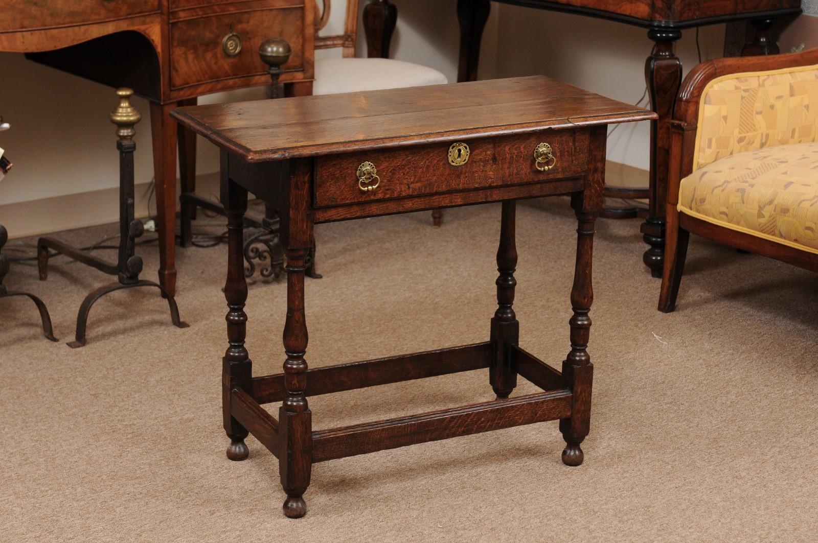 A 18th century English oak side table featuring drawer in frieze with brass hardware, turned legs joined by box stretcher and rounded feet.
 