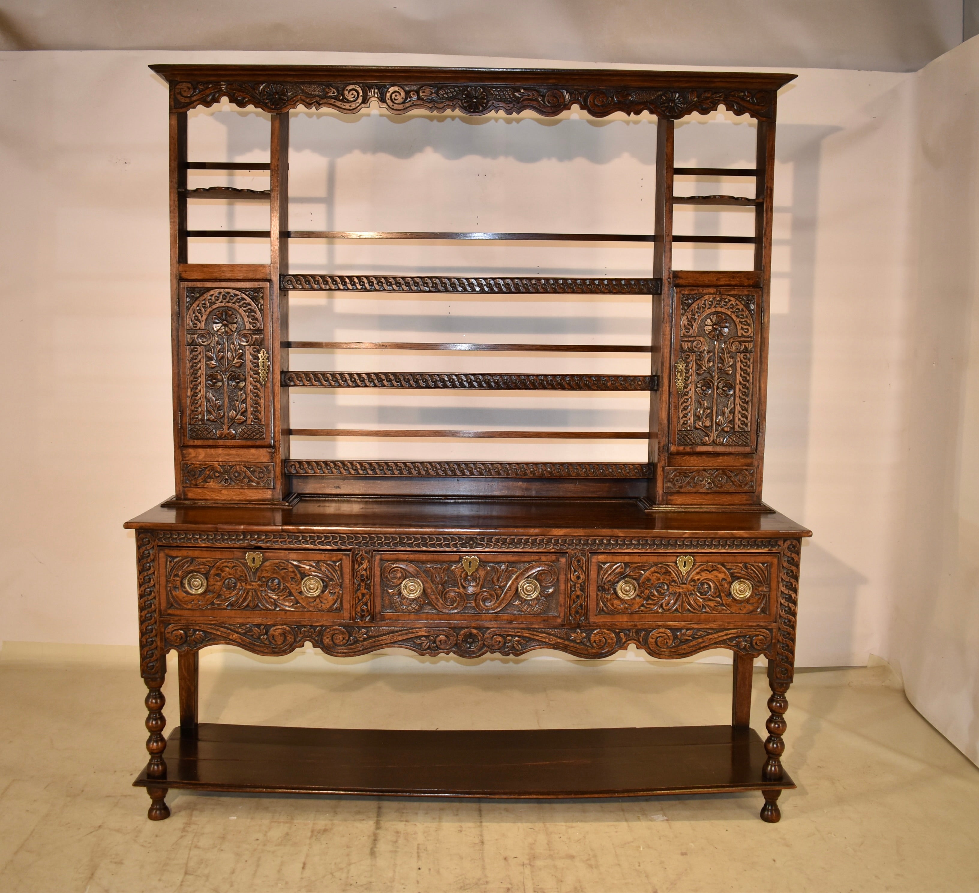 18th century Welsh dresser made from oak.  The top has a lovely crown molding over a scalloped frieze, which is highly carved with lovely decoration.  The back of the dresser has open shelving, with rails along the back, and hand carved shelf