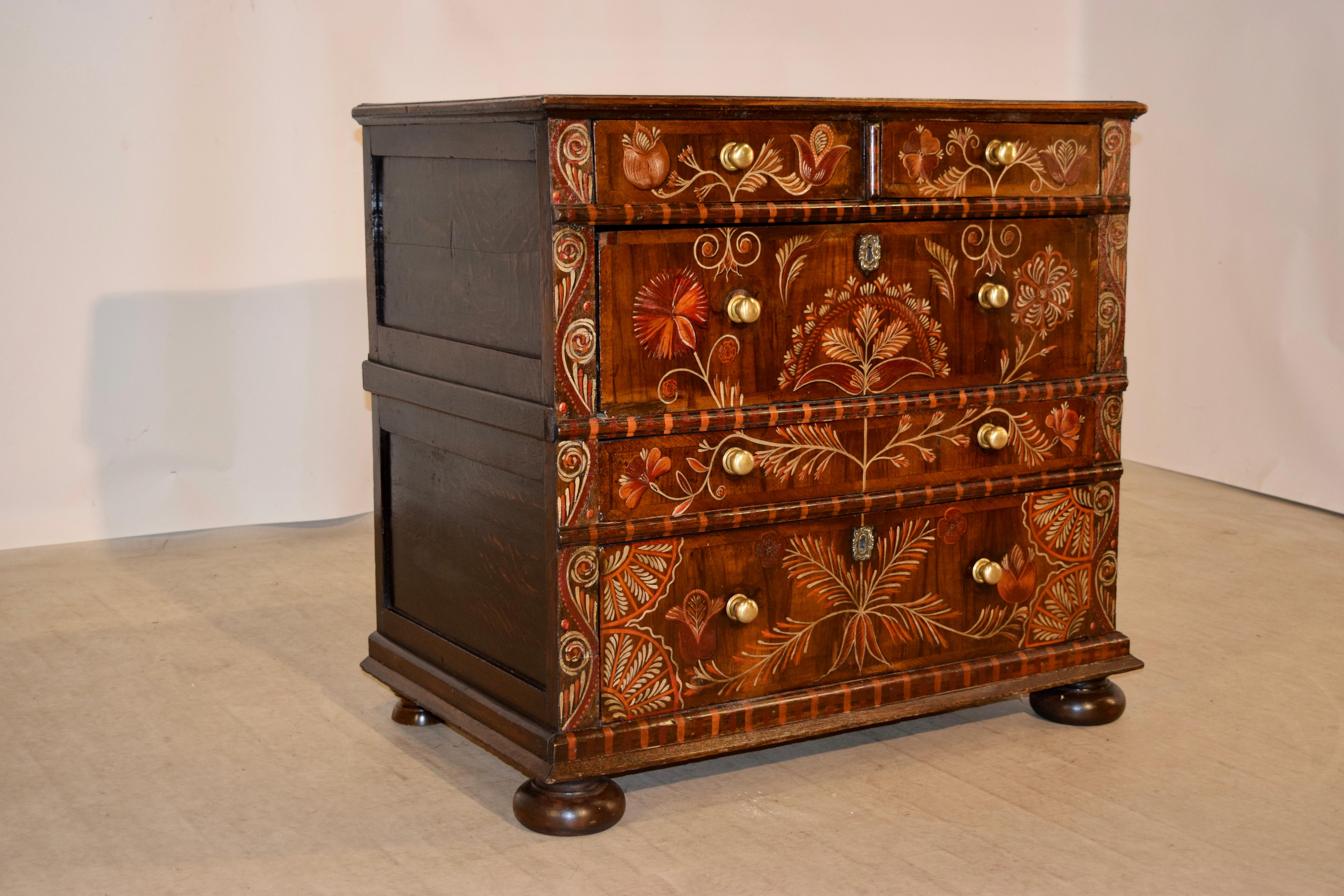 18th century chest of drawers from England with recent decoration in the style of original Jacobean decoration. The top has a bevelled edge and follows down to panelled sides and two small drawers over three larger drawers, of various sizes, all