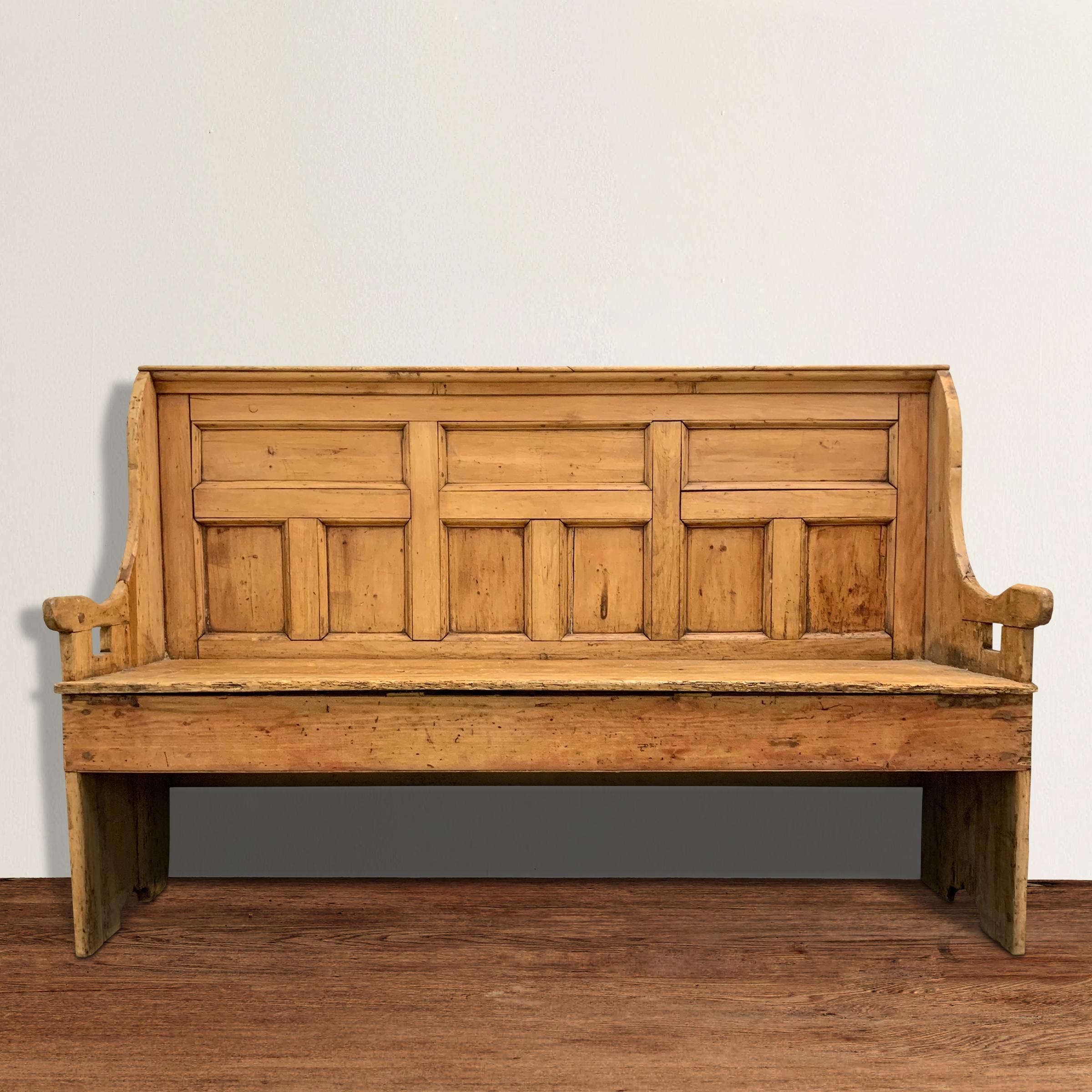 A charming 18th century English pine settle with a tall paneled back, a generous deep seat, and quirky arms with a well-worn finish bestowed from over two hundred years of use.