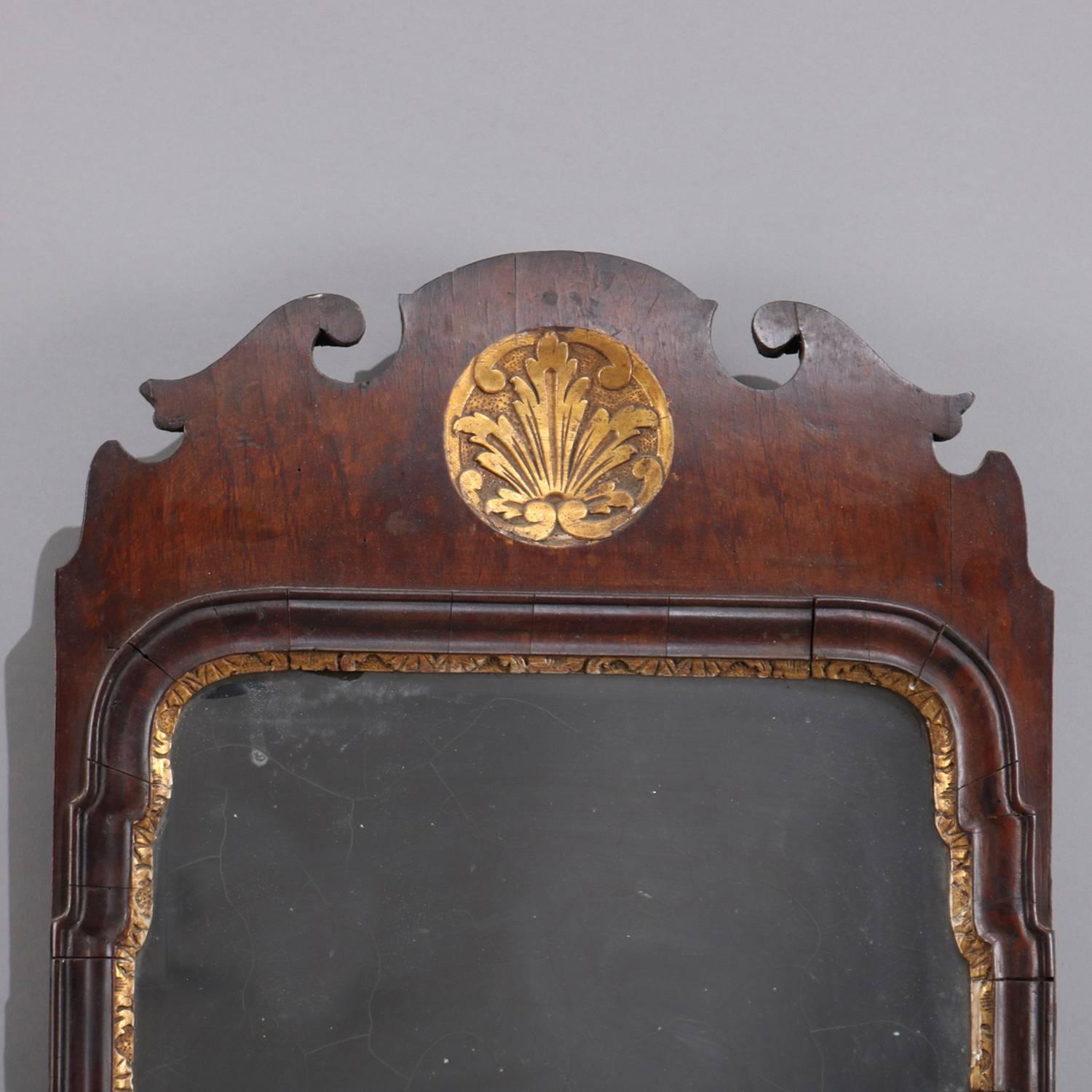 18th century English Queen Anne wall mirror features scroll cutout mahogany frame with carved and gilt palmette central reserve on crest, shaped mirror with carved and gilt bordering, fragile and as-is, circa 1730

Measures: 50