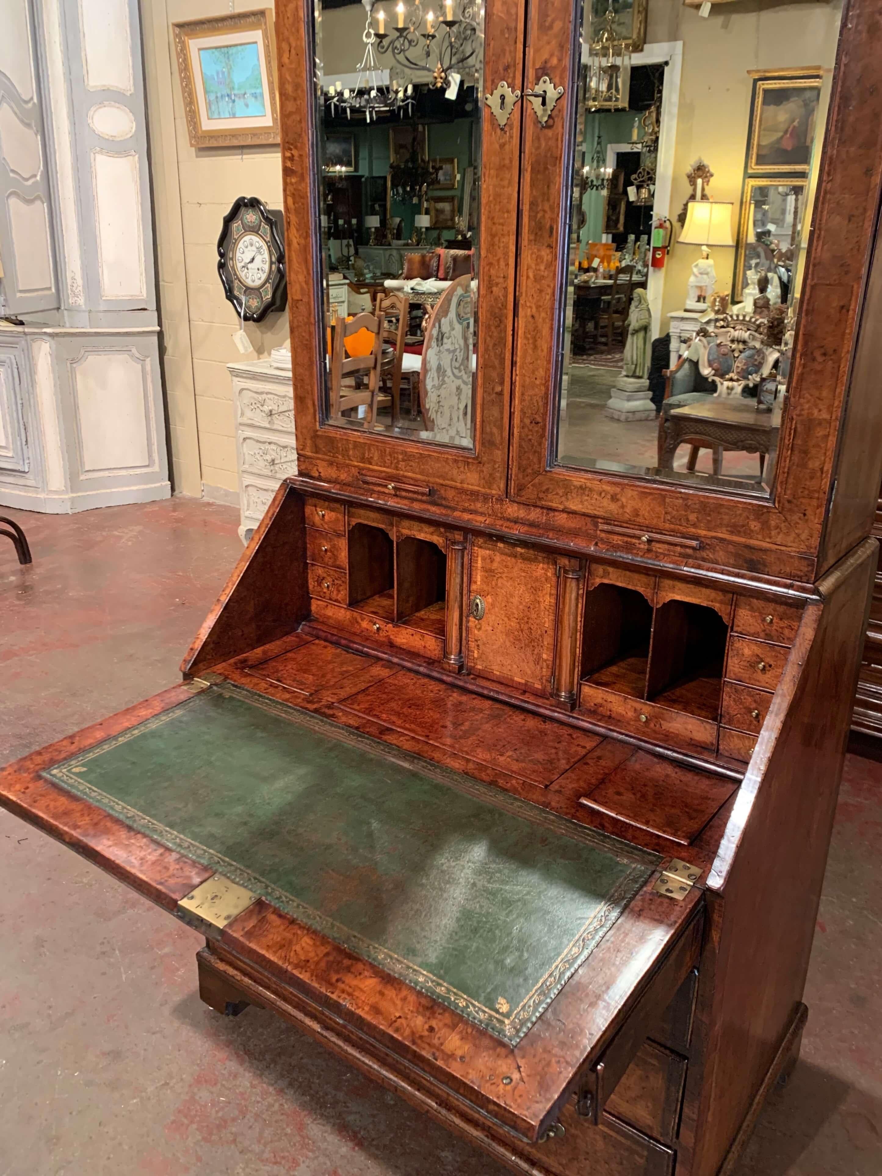 Created in England circa 1720, and made of walnut and burl, this elegant antique secretary is built in two sections; the upper section boasting a desirable bonnet Top is decorated with three carved finials. The beveled mirrored doors Open to reveal