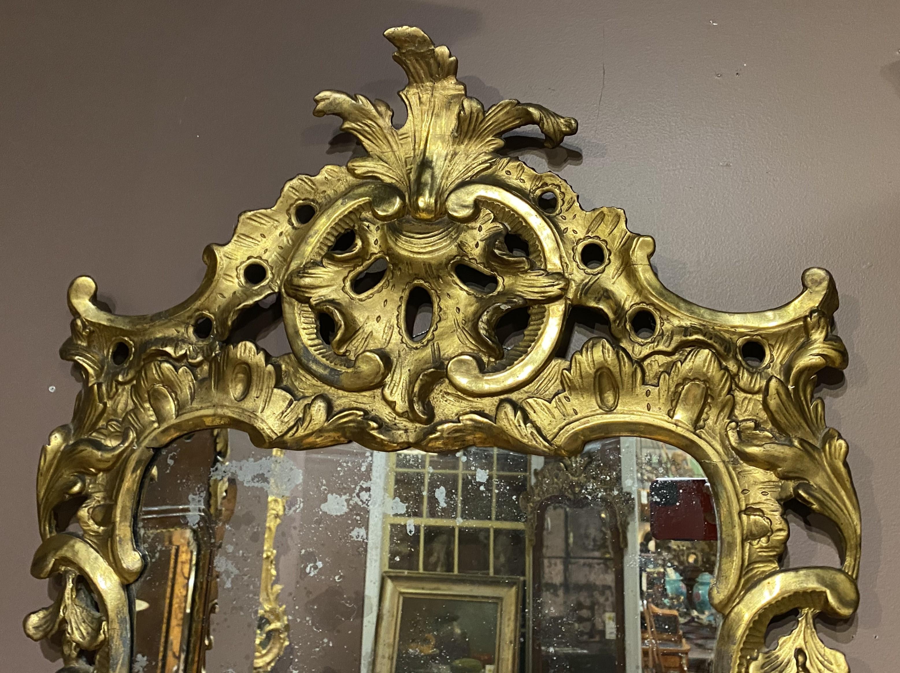 Un exemple impressionnant de  un miroir mural rococo anglais avec un cadre en bois doré ajouré et sculpté à la main avec un décor de rinceaux et de feuillages, et orné d'une crête de feuillage prononcée, le tout en très bon état général, avec