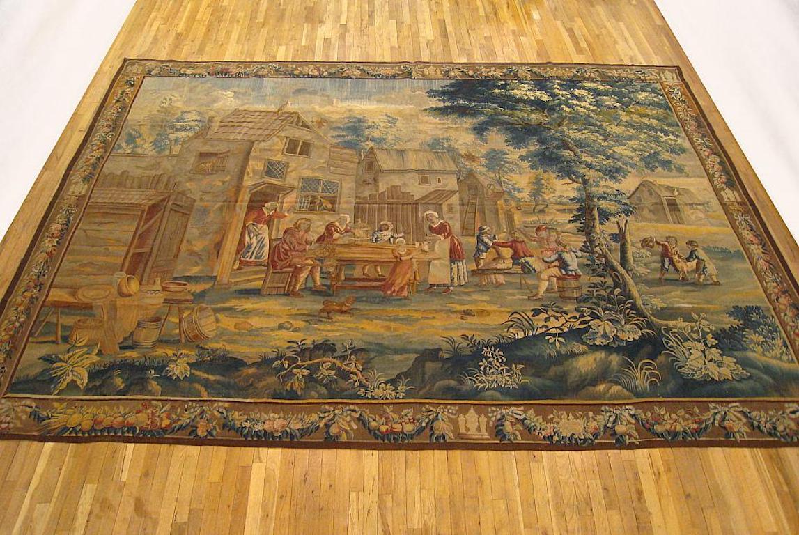 An English Baroque rustic tapestry from the second quarter of the 18th century, centrally woven, featuring a rustic scene in the manner of David Teniers II, in which several villagers make merry in front of a cottage that has a cat in one window and