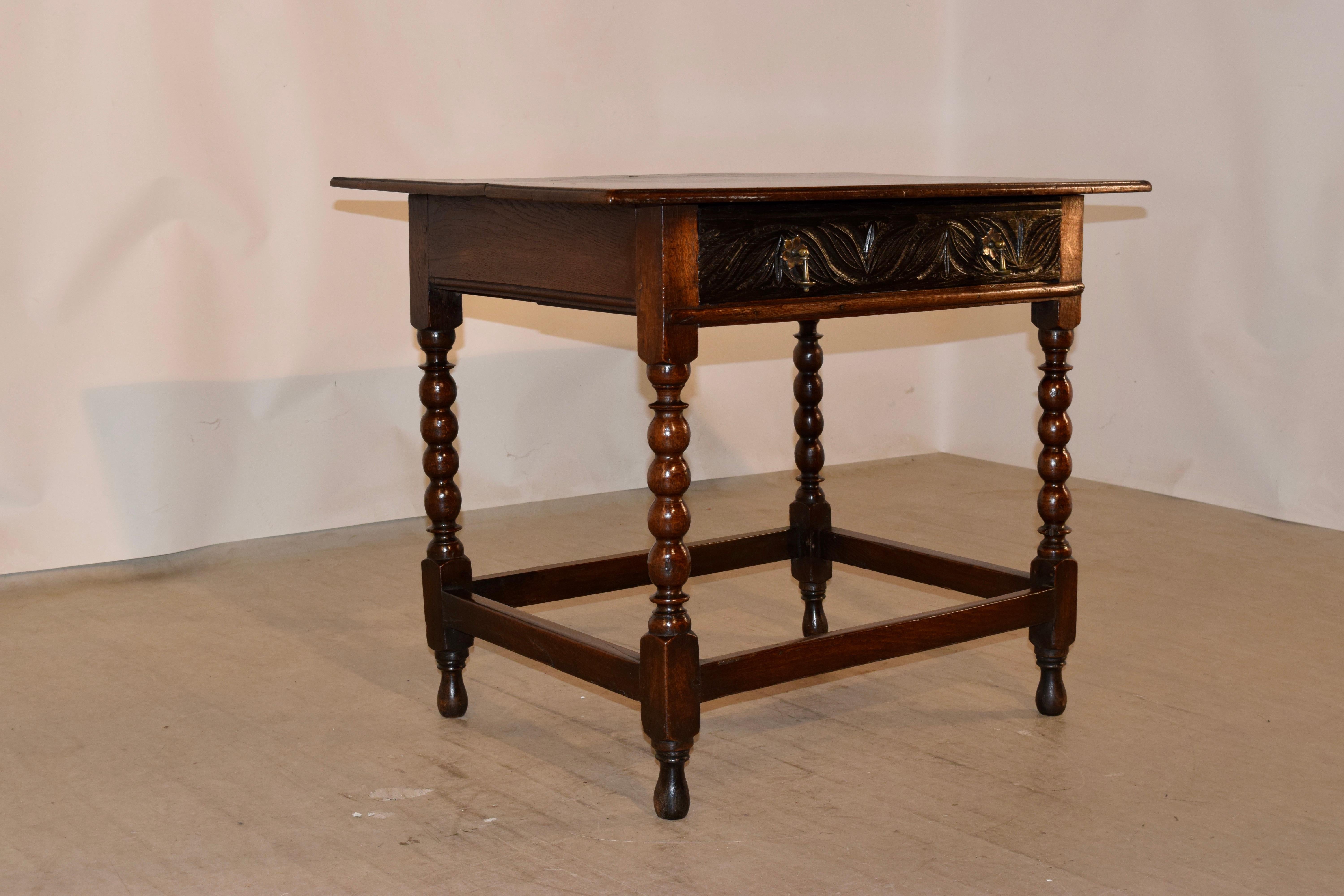 18th century English side table made from oak. The top has a beveled edge around the top, which has lovely graining detail. This follows down to simple sides and a single drawer with a carved decorated drawer front and hand-turned bobbin shaped