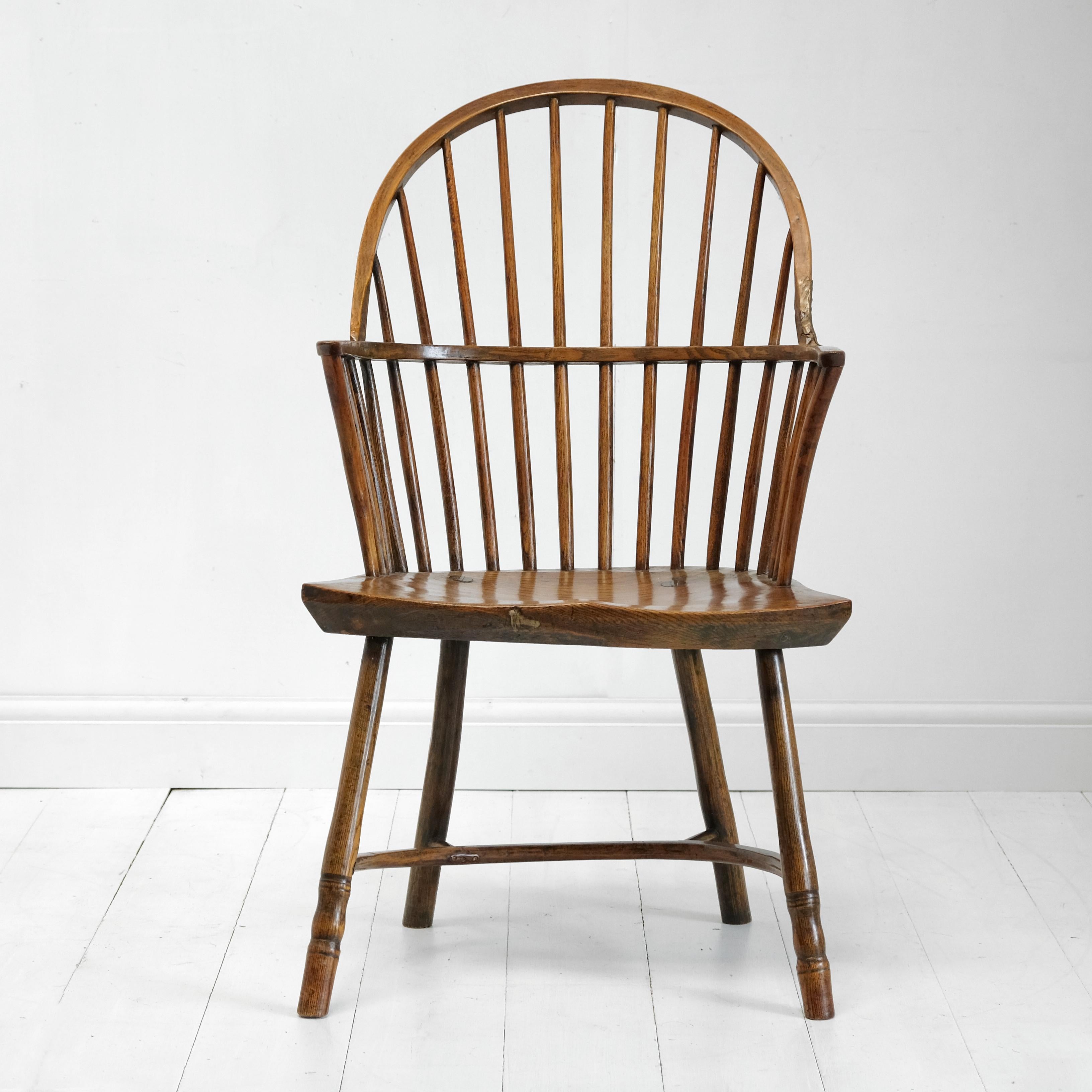 An 18th century stick back Windsor chair in elm and ash with traces of original green paint. The simple legs are united by a crinoline stretcher and are morticed into the shaped elm seat. Simple stick back with hooped armrest and bent arm supports.