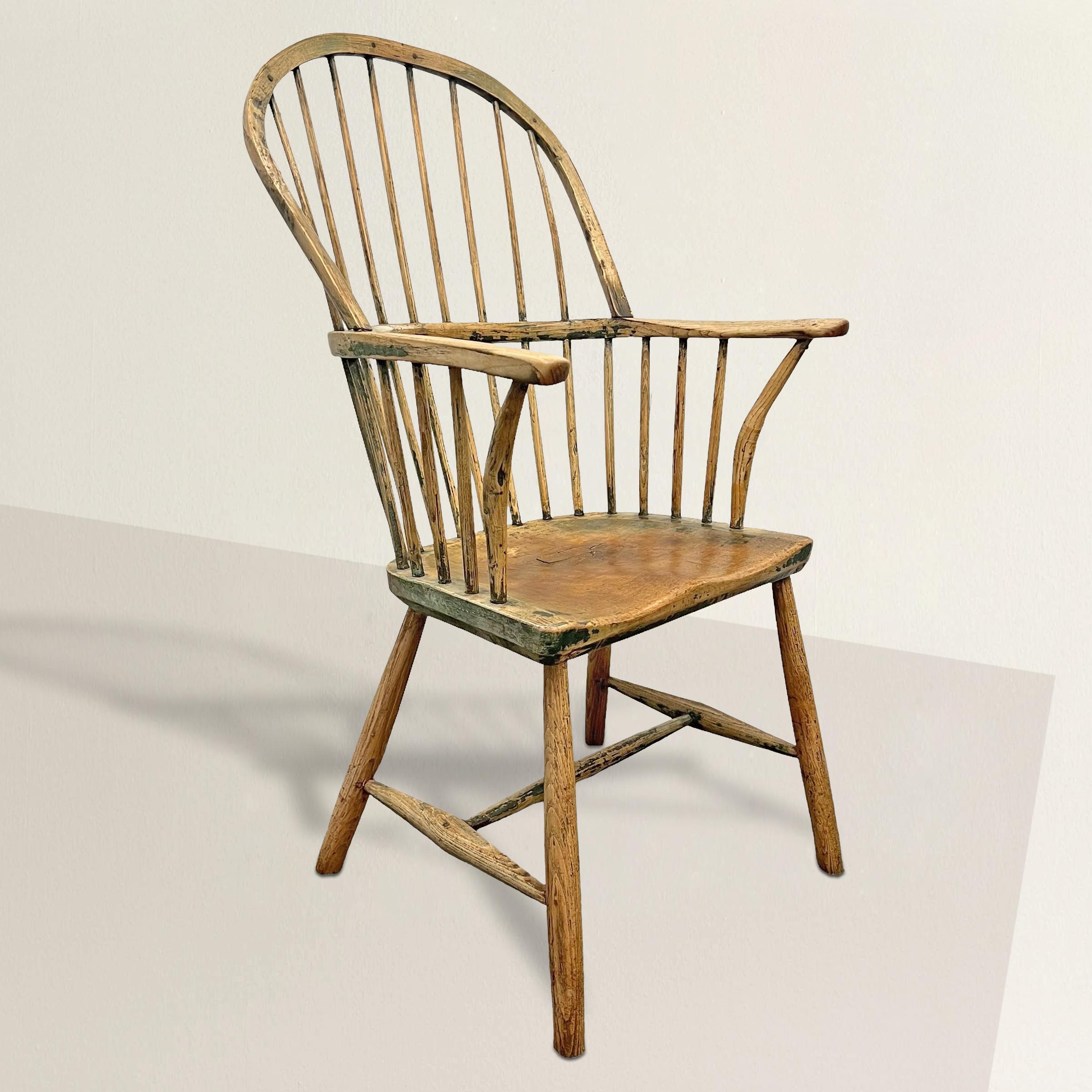 This 18th-century English elm wood stickback Windsor armchair presents an aura of understated elegance and historical depth. Stripped of its original paint, the chair now bares the natural beauty of elm wood, revealing the warm, rich tones and