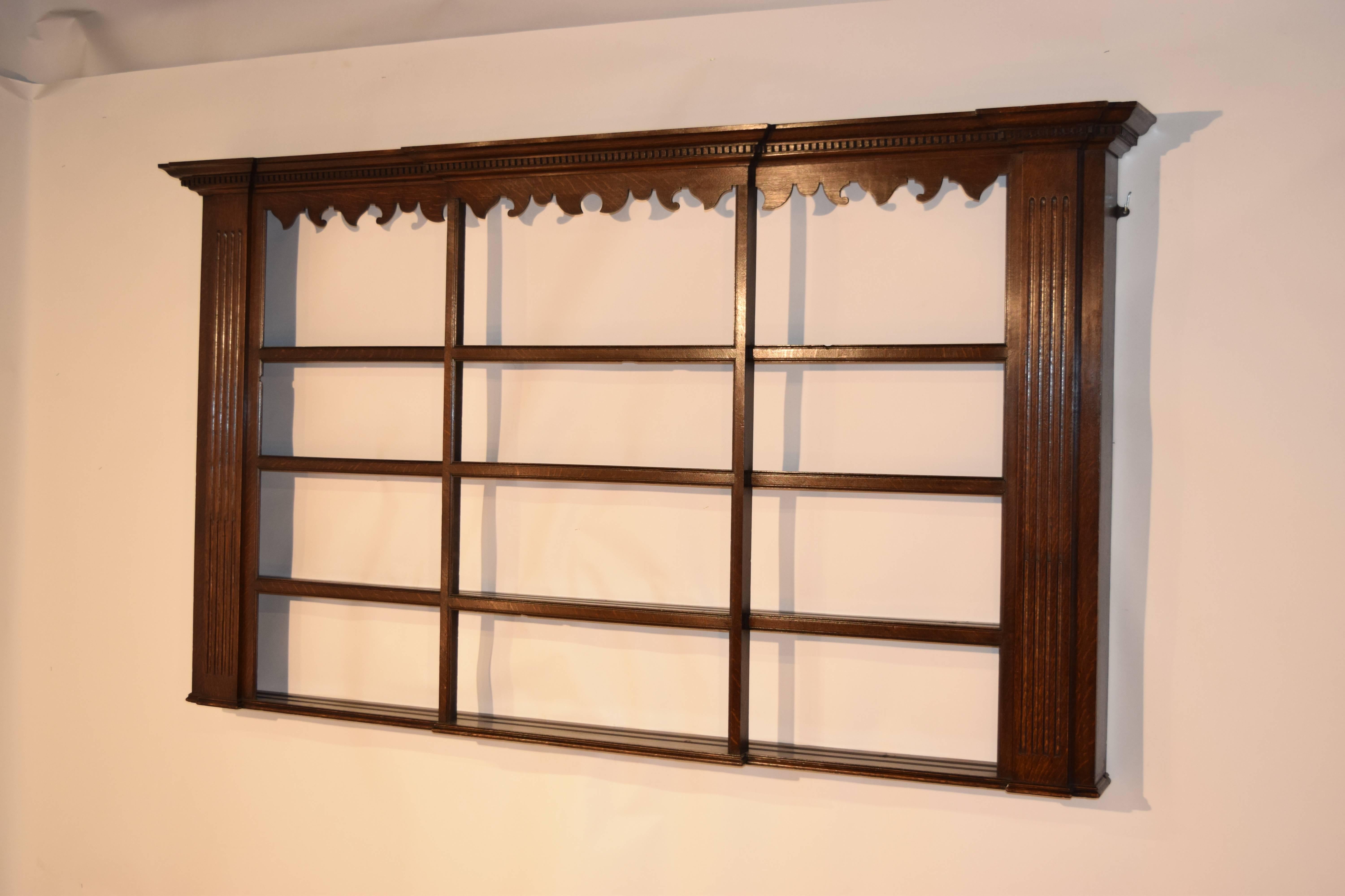 Late 18th century Georgian oak wall shelf with stepped crown molding which has dental detail as well, following down to a lovely hand scalloped apron over four shelves. the shelves are flanked on the sides with fluted columns. Beautiful color and