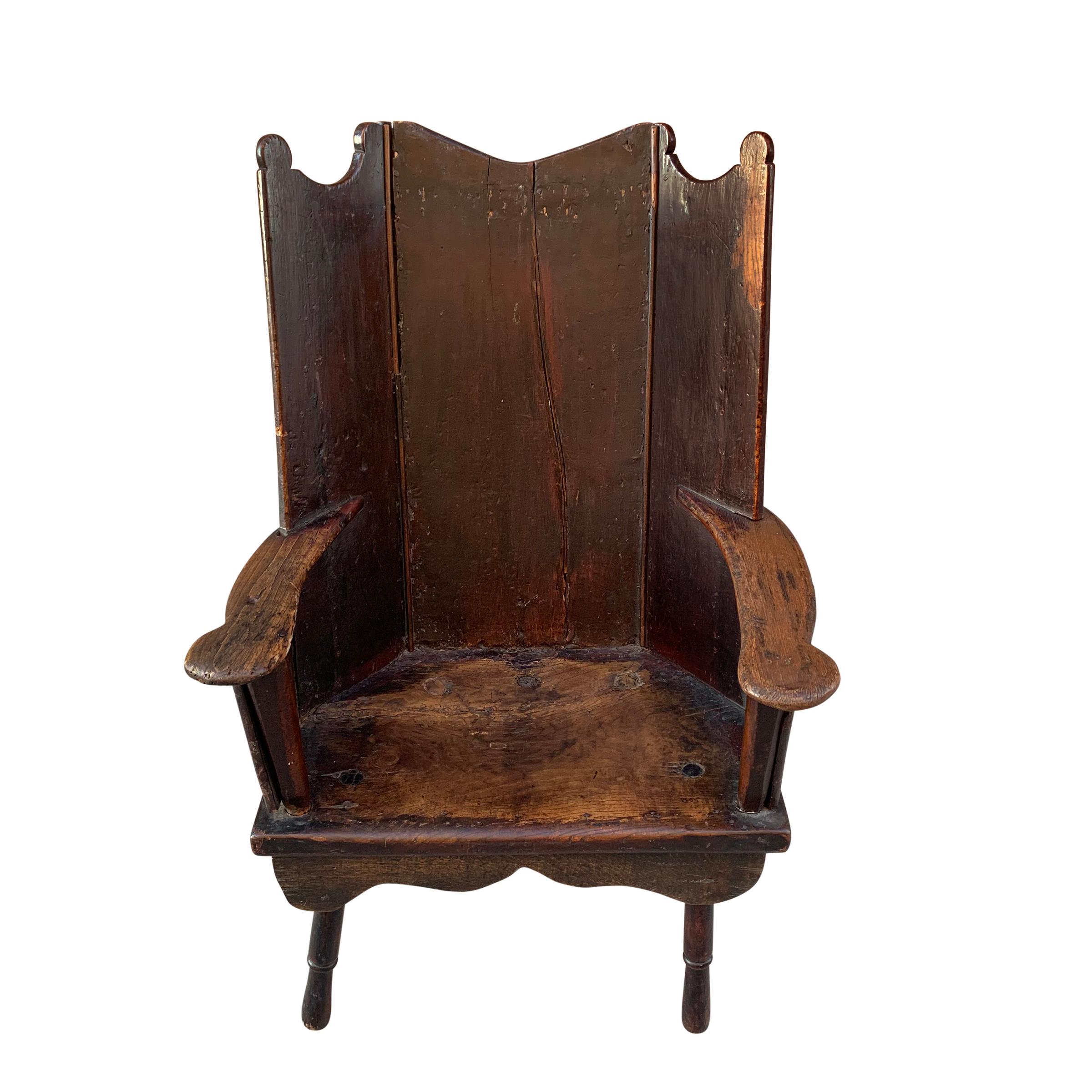 An extraordinary 18th century English oak wingback chair having a back constructed of three oak panels with scalloped top, and straight flat arms with rounded ends, through turned front legs and more recent back legs. The seat has a fantastic patina