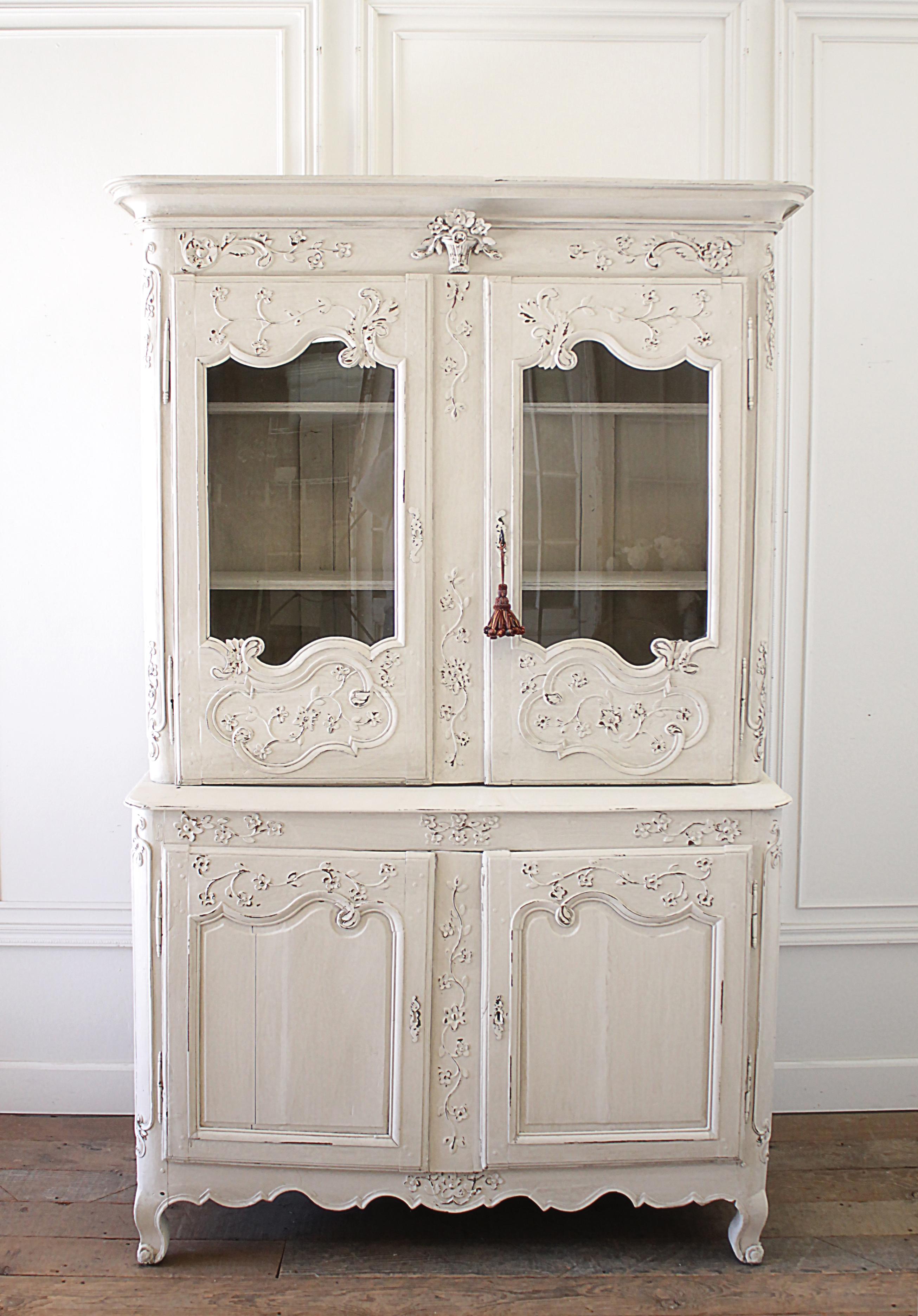 Antique Louis XV buffet deux corps from the Normandy region of France in beautifully painted soft white oakwood with distressed patina, intricately hand carved doors and updated with glass replacements for the panels. Nicely carved with flower