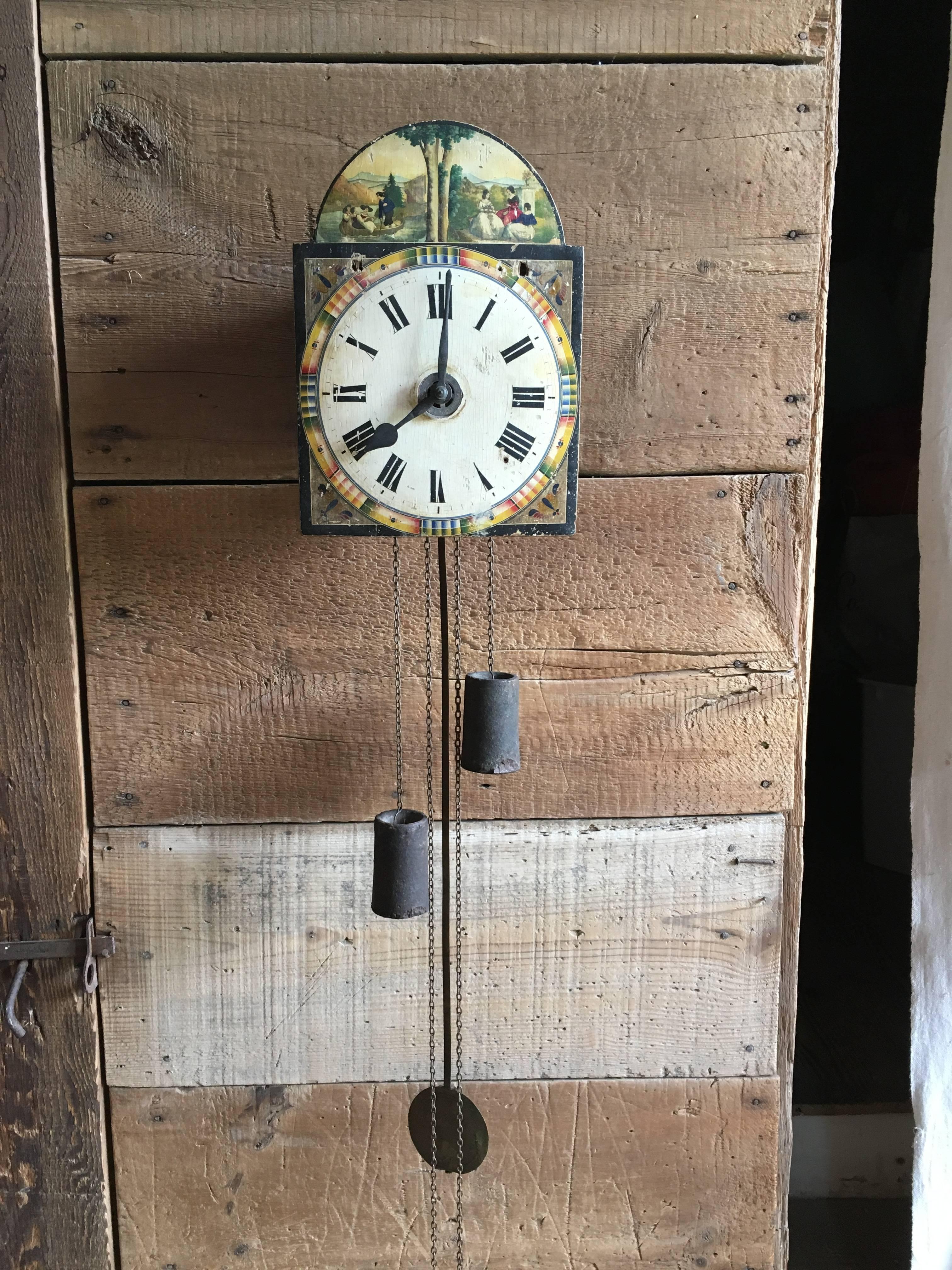 A charming French or German 18th century wall clock without case, the wood face with a painted courting scenes, the clock appears to be complete and working but needs to be cleaned and balanced. Chimes on hour and half. 
Pendulum adds 30” to height.