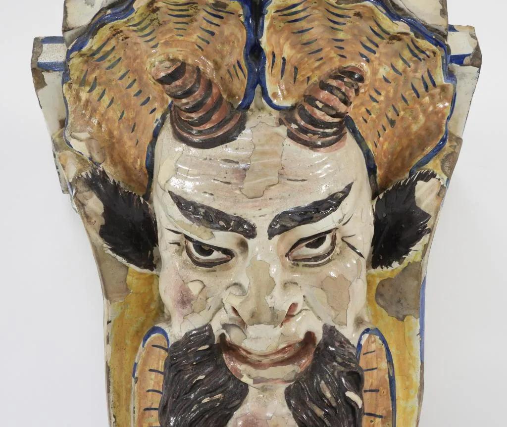 A late 18th century faience shelf or wall bracket in the form of a demon's face, losses to glaze in areas, with wear and chips overall.