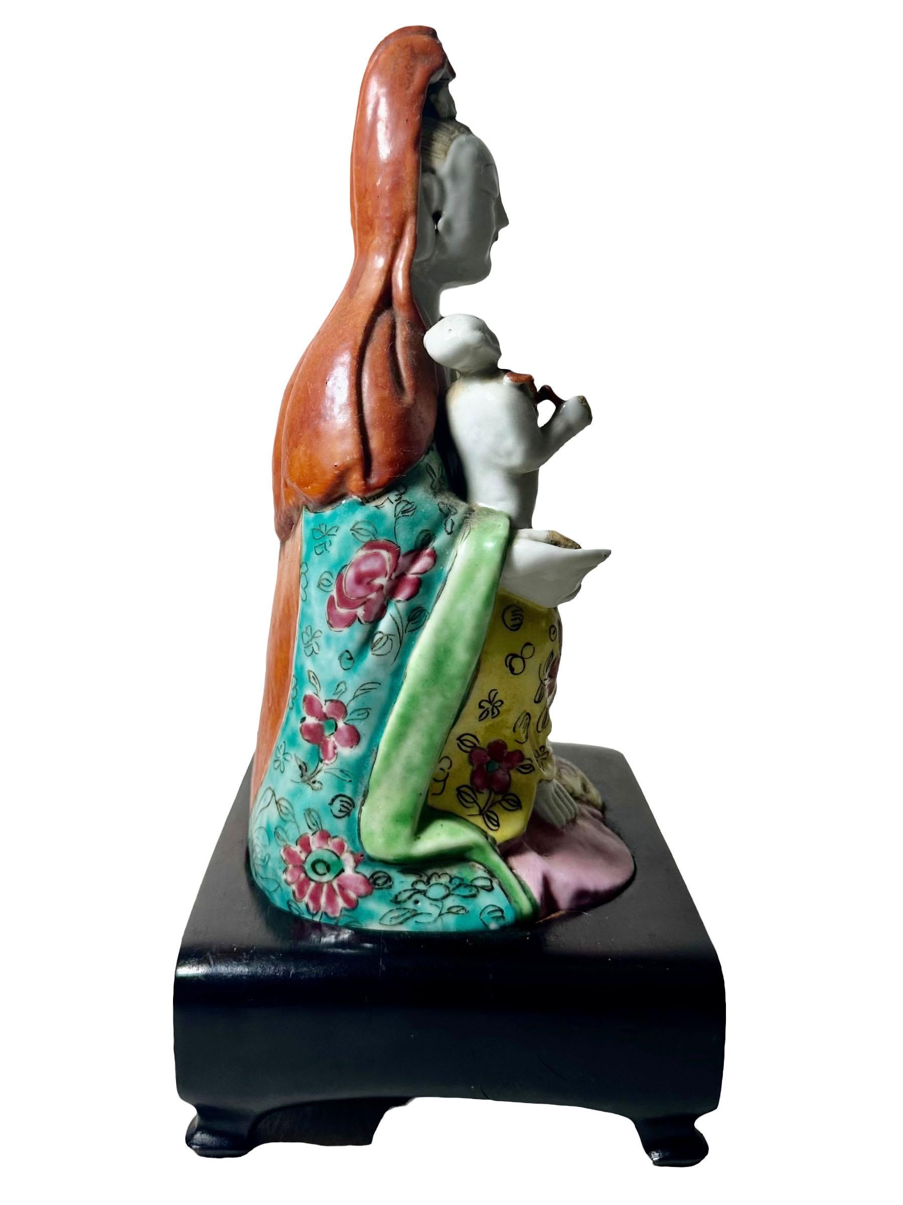 Una statuetta Famille Rose del XVIII secolo con un bambino seduto su un supporto in palissandro personalizzato. Il supporto risale agli anni '20-'30 ed è alto 5 cm. La statua in sé misura quattro centimetri e mezzo di larghezza, tre centimetri e
