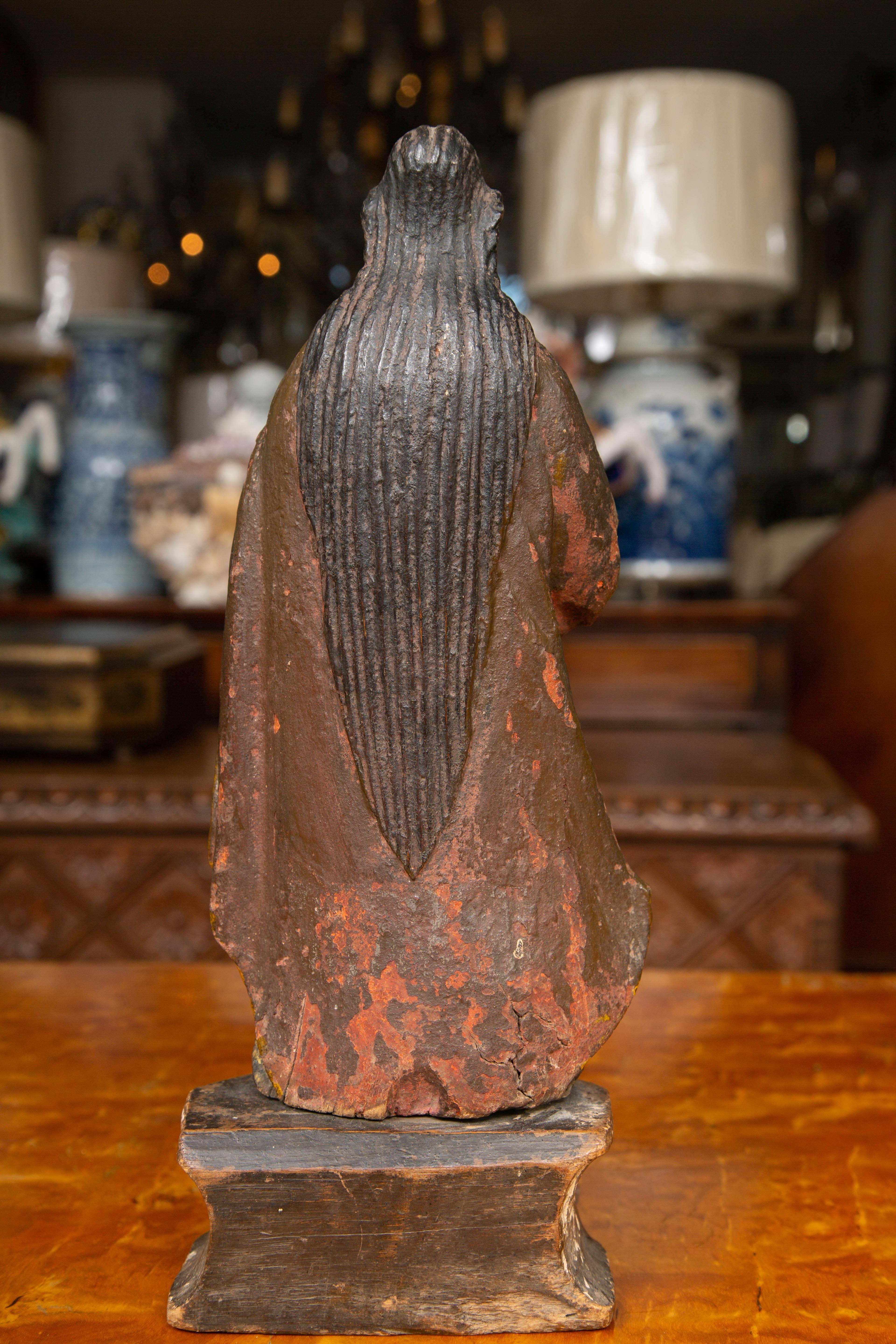 This is a polychromed hand carved figure of a religious figure. The saint is garbed in a flowing robe standing on a pedestal. The polychromed finish is a mixture of blues, yellow, whites and muted red. The naturally worn and patinated finish offers
