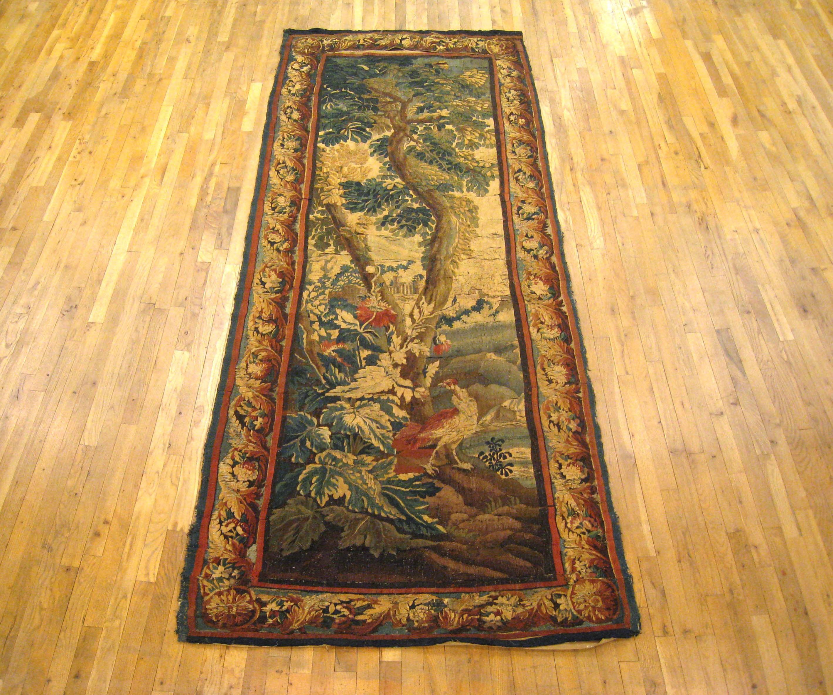 A Flemish verdure landscape tapestry panel from the 18th century. This handwoven antique wall hanging features a verdure scene with a beautiful red bird in front of a verdant tree near a lake. In the background, an elegant architectural building can