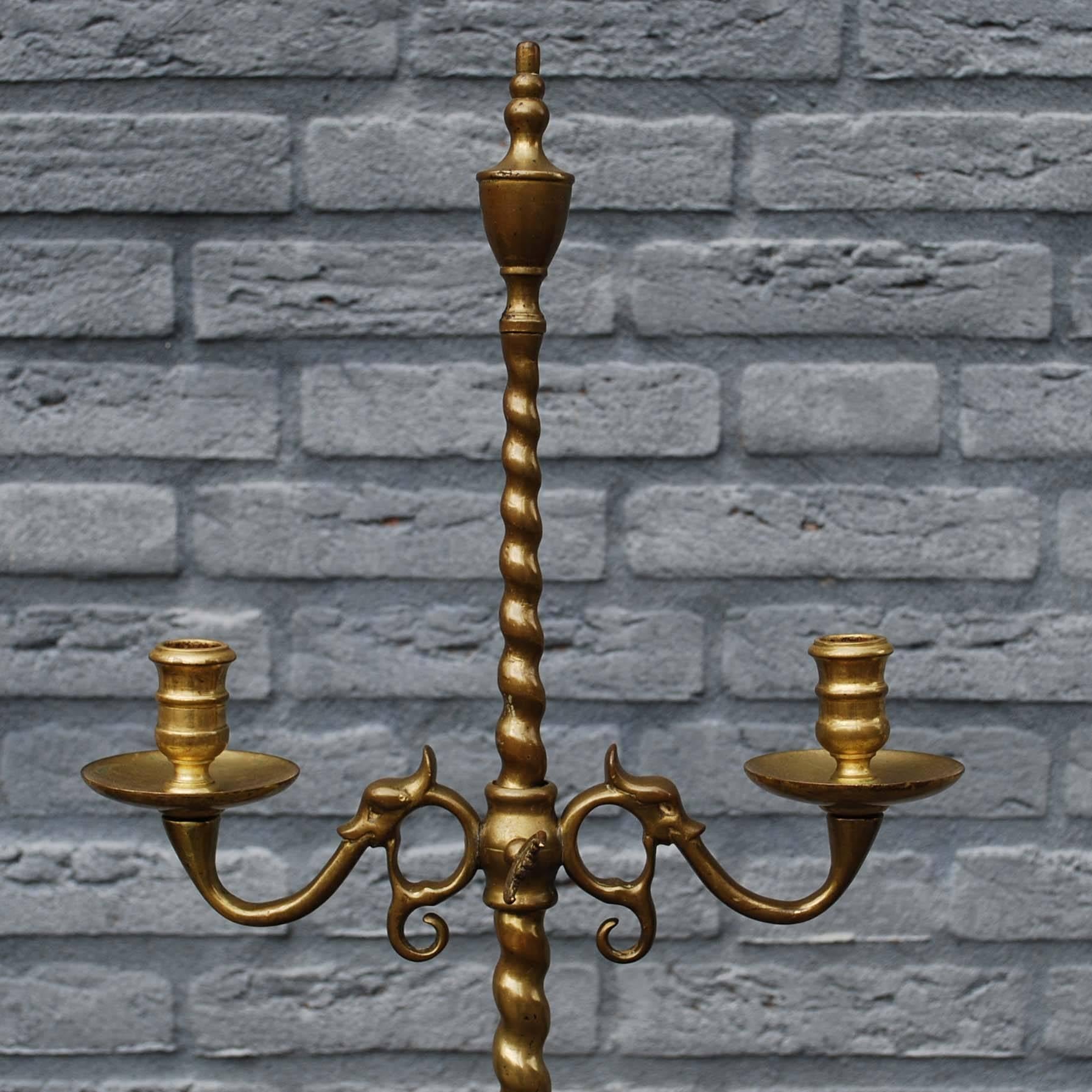 Beautiful hand-forged brass candleholder or candelabra.
It has a tripod base with half turned twist legs that supports a solid turned twist column with a finial urn on top.
It features two rotating candleholders that swivel over the column.
It