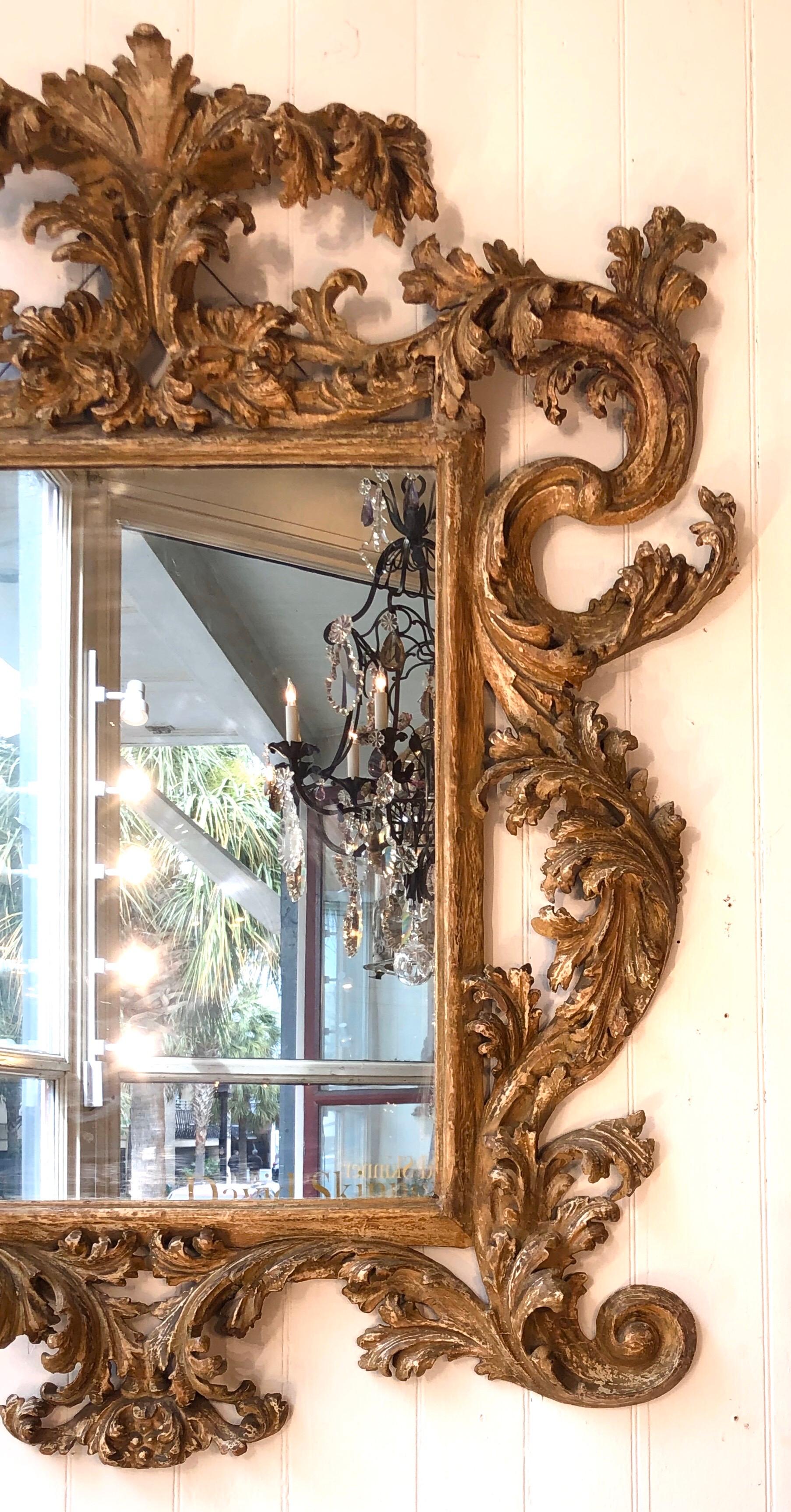 This Palatial Italian 18th century mirror has a beautiful antique worn gilt patina with shades of white and cream coming through. The foliage and scrolls that frame the mirror are classically craved. The crusty finish on this Baroque mirror is