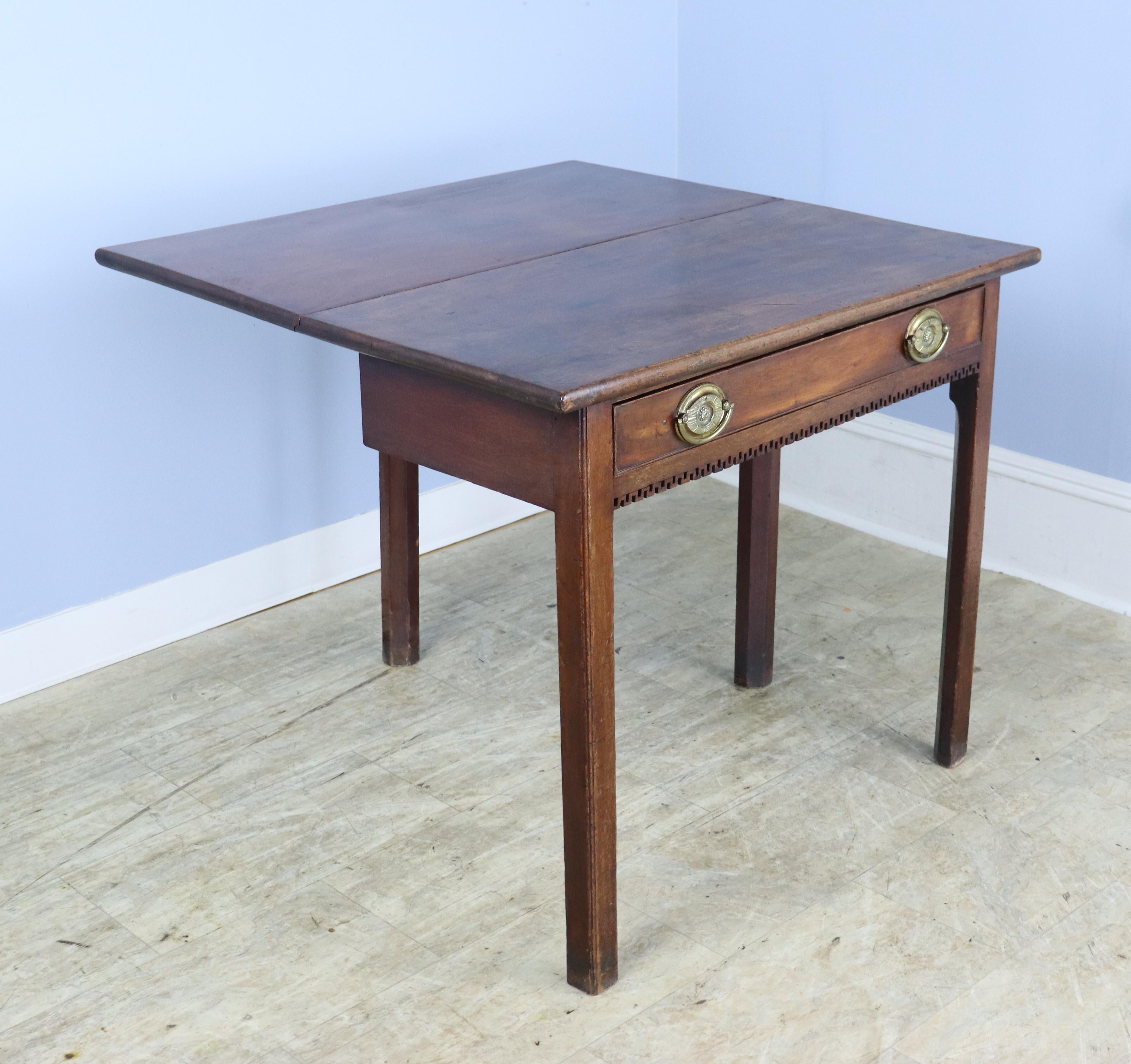 A charming Georgian mahogany card or tea table in mellow mahogany. The piece folds out to double its usable surface, and can be stored in the closed position as an attractive side table. The hand cut dentil molding at the base of the drawer is the