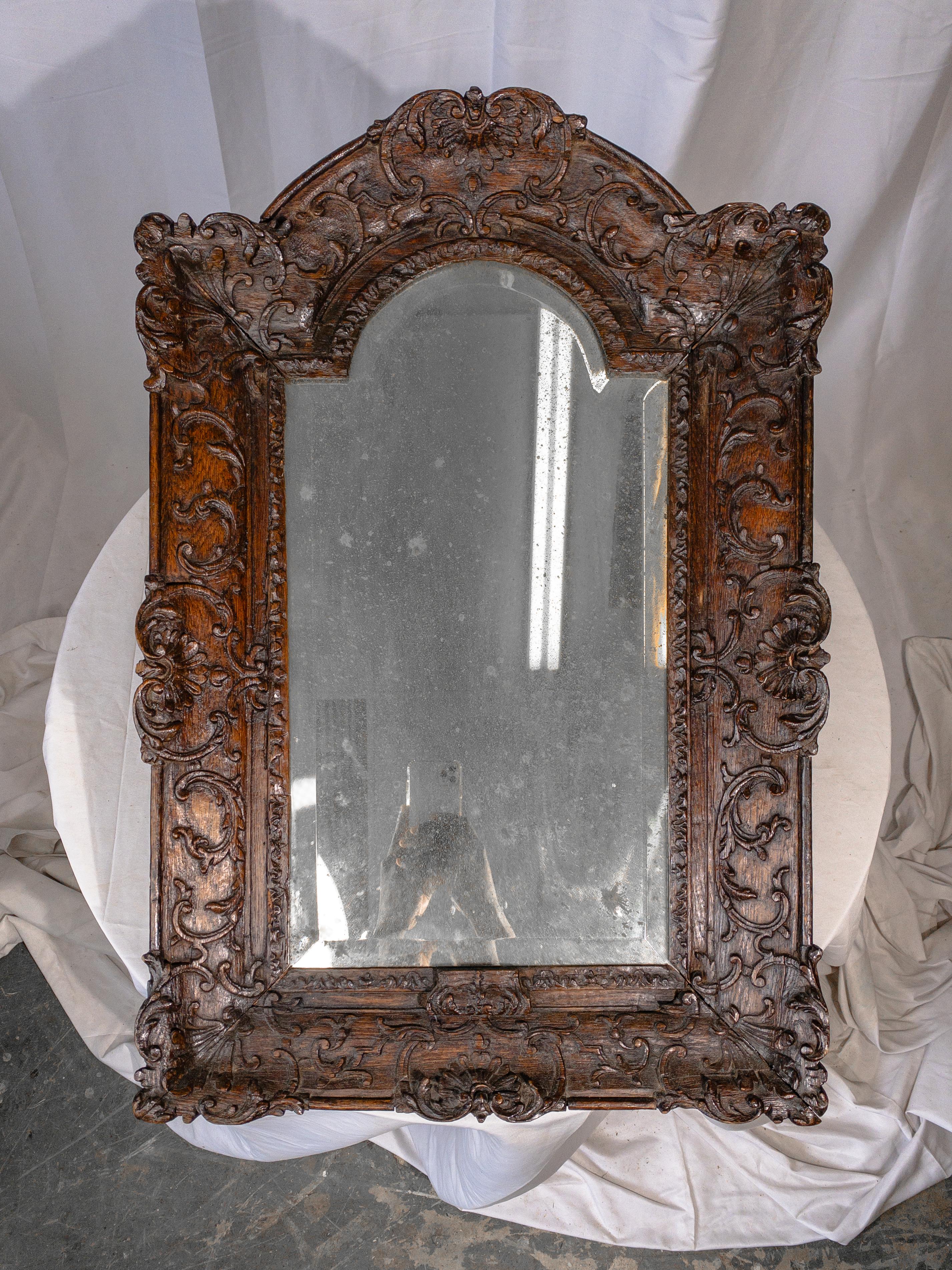 This 18th-century foxed mirror, nestled within a meticulously hand-carved wooden frame, epitomizes the elegance and craftsmanship of the late Renaissance period. The frame itself is a testament to artisanal skill, with intricate carvings that evoke