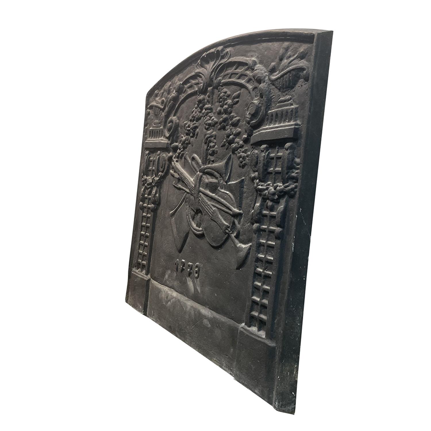 
An antique French fireback with flanking trellis adorned with garlands and an anchored motif with musical instruments, in good condition. Minor fading, due to age. Wear consistent with age and use. Dated 1778, France.