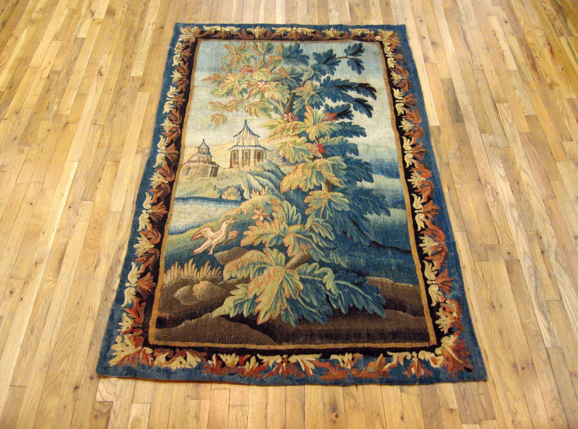 A French Aubusson chinoiserie verdure tapestry, 18th century. A small bird to the left, an acanthus bush in the center, and pagodas in the left distance, within a symmetrical scrolling foliate border. Wool with silk inlay. Measures: 6’9” H x 4’0”