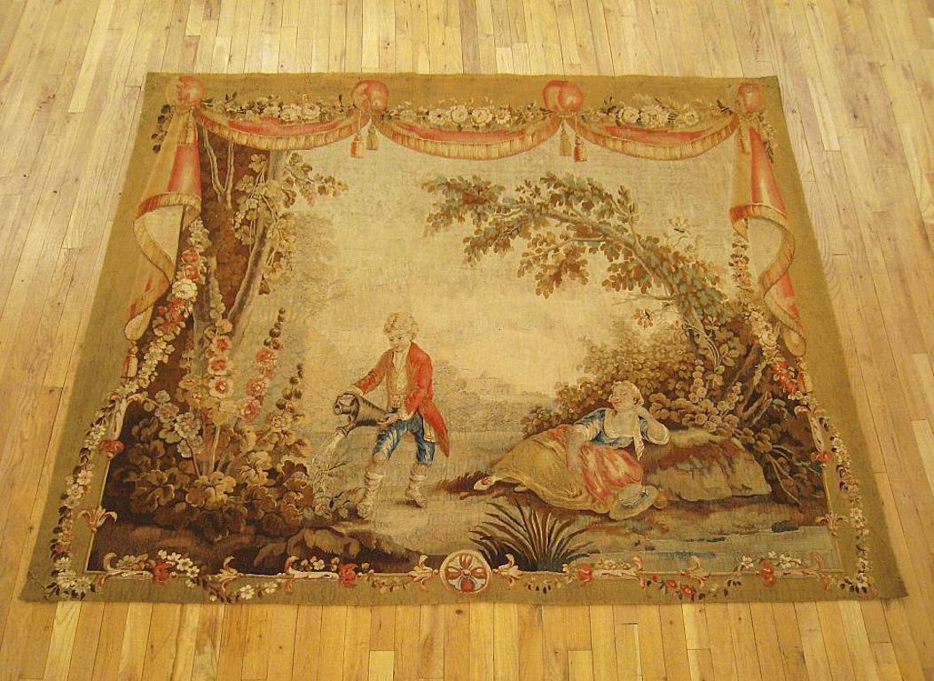 A Louis XV French Aubusson pastoral tapestry from the second half of the 18th century, after designs by Jean-Baptiste Huet, centrally woven with a pastoral scene in a picturesque courtyard, featuring a young swain watering the flowers while a damsel