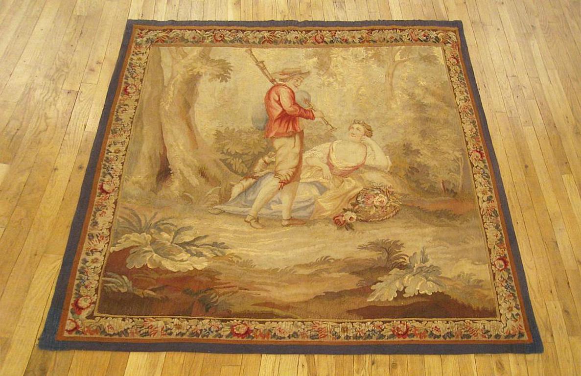 A French Aubusson genre tapestry from the 18th century, featuring a rustic scene in which a youth plays his instrument for his damsel, who is reposing in the clearing of a forest. Enclosed within a scrolling foliate border. Wool with silk inlay.