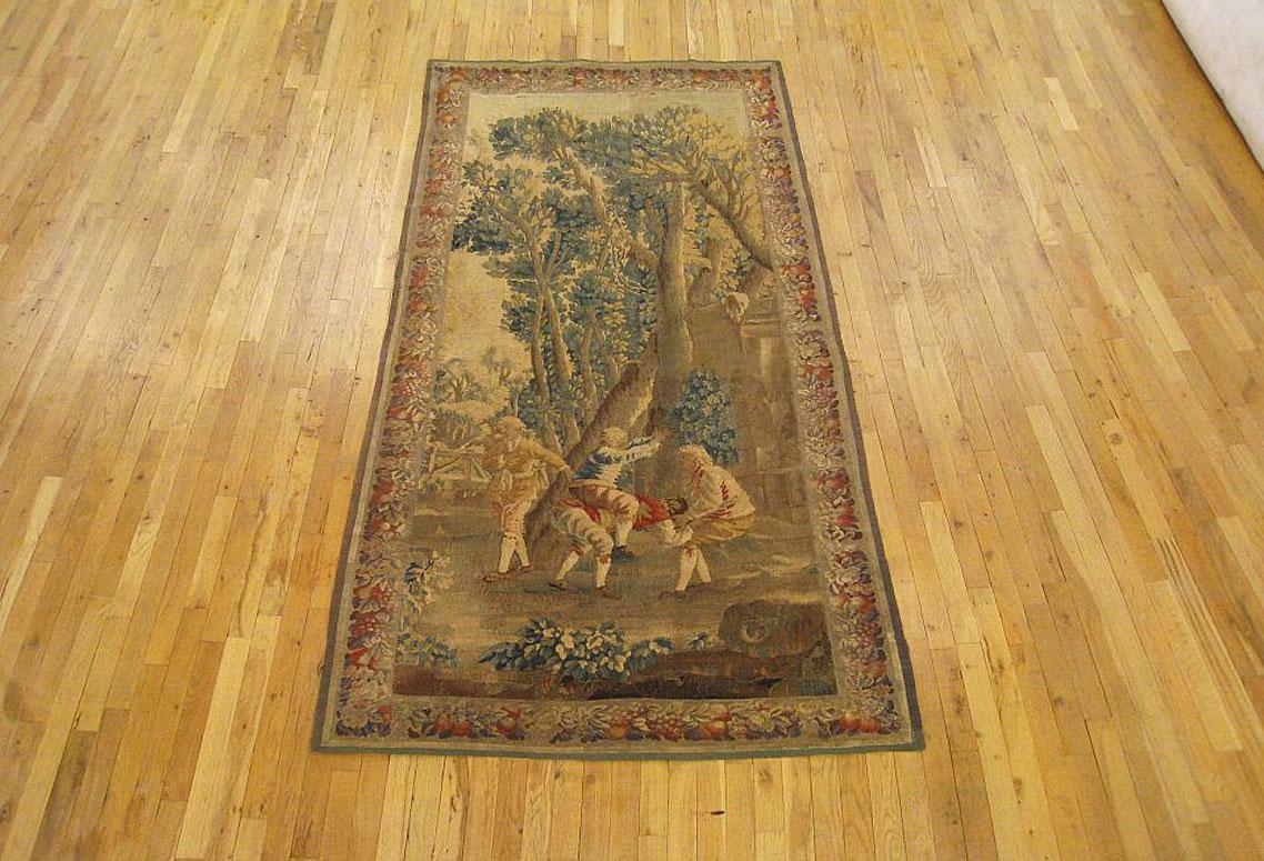 Une tapisserie rustique française d'Aubusson du 18e siècle, représentant un paysage boisé dans lequel plusieurs jeunes jouent à saute-mouton. Le tout est entouré d'une bordure défilante d'éléments fruitiers et floraux. Laine avec incrustation de